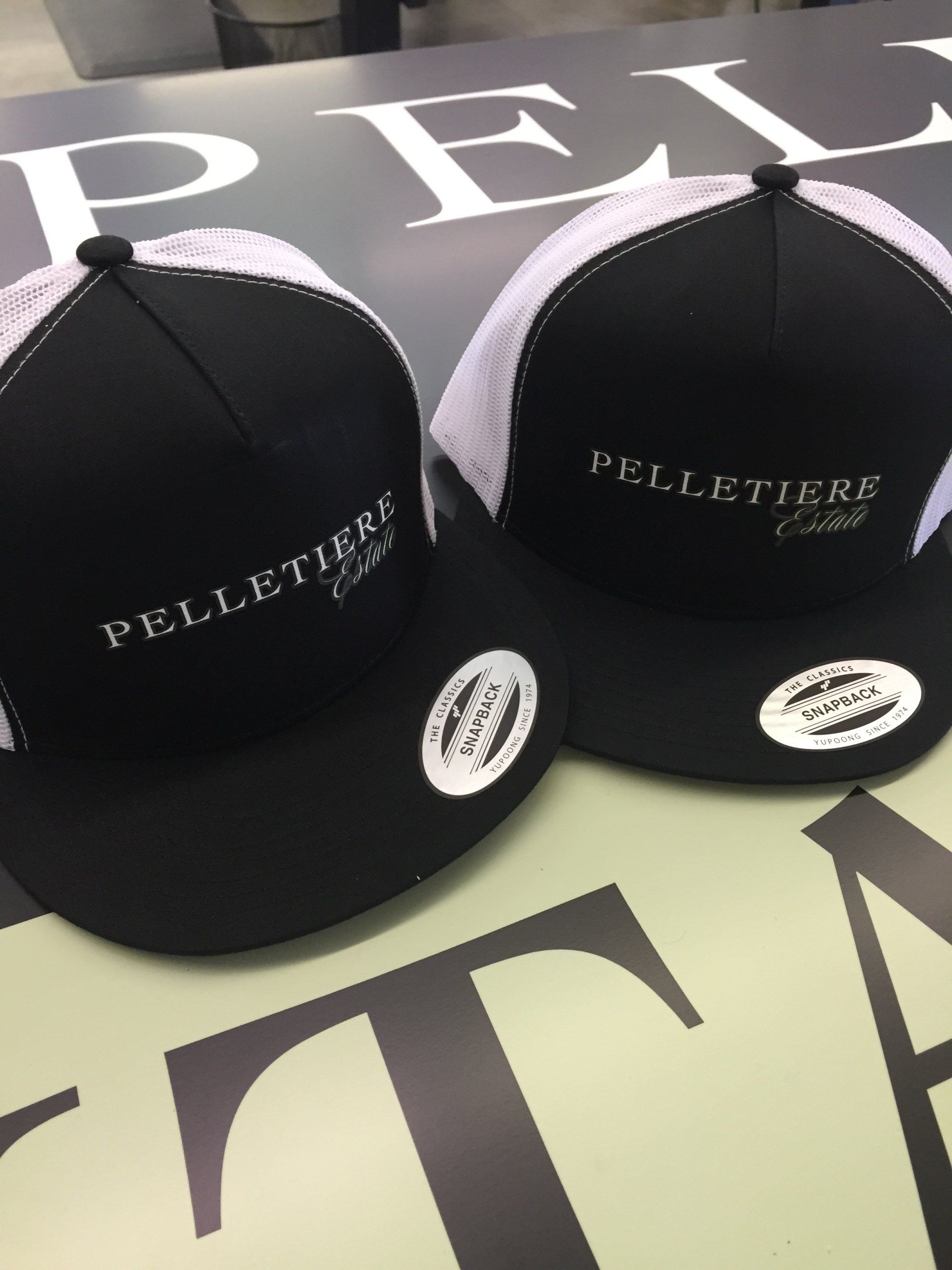 Two black Telleteria caps with white logos on a branded display background