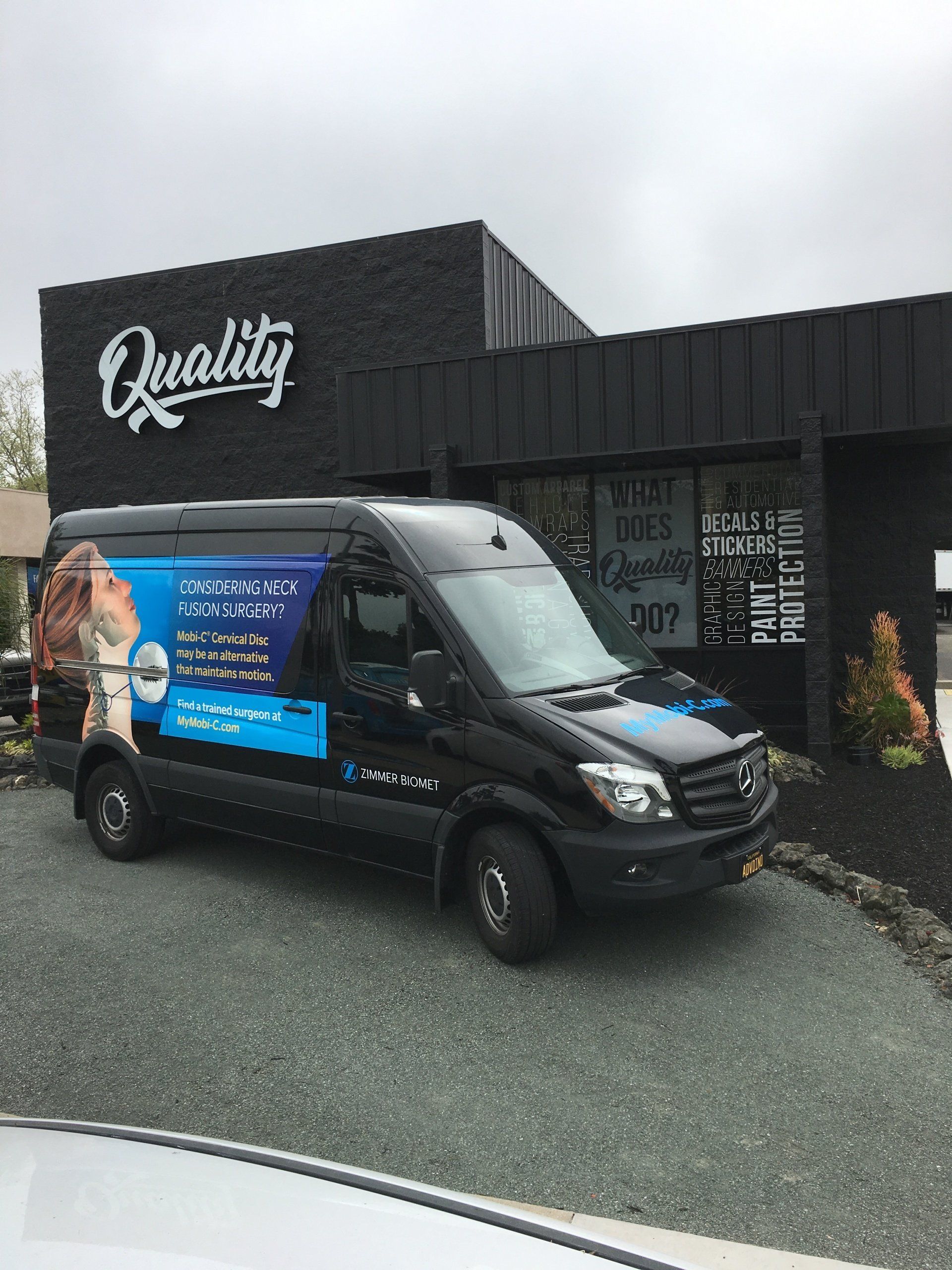 Black van with blue advertising parked outside a dark storefront labeled “Quality.”