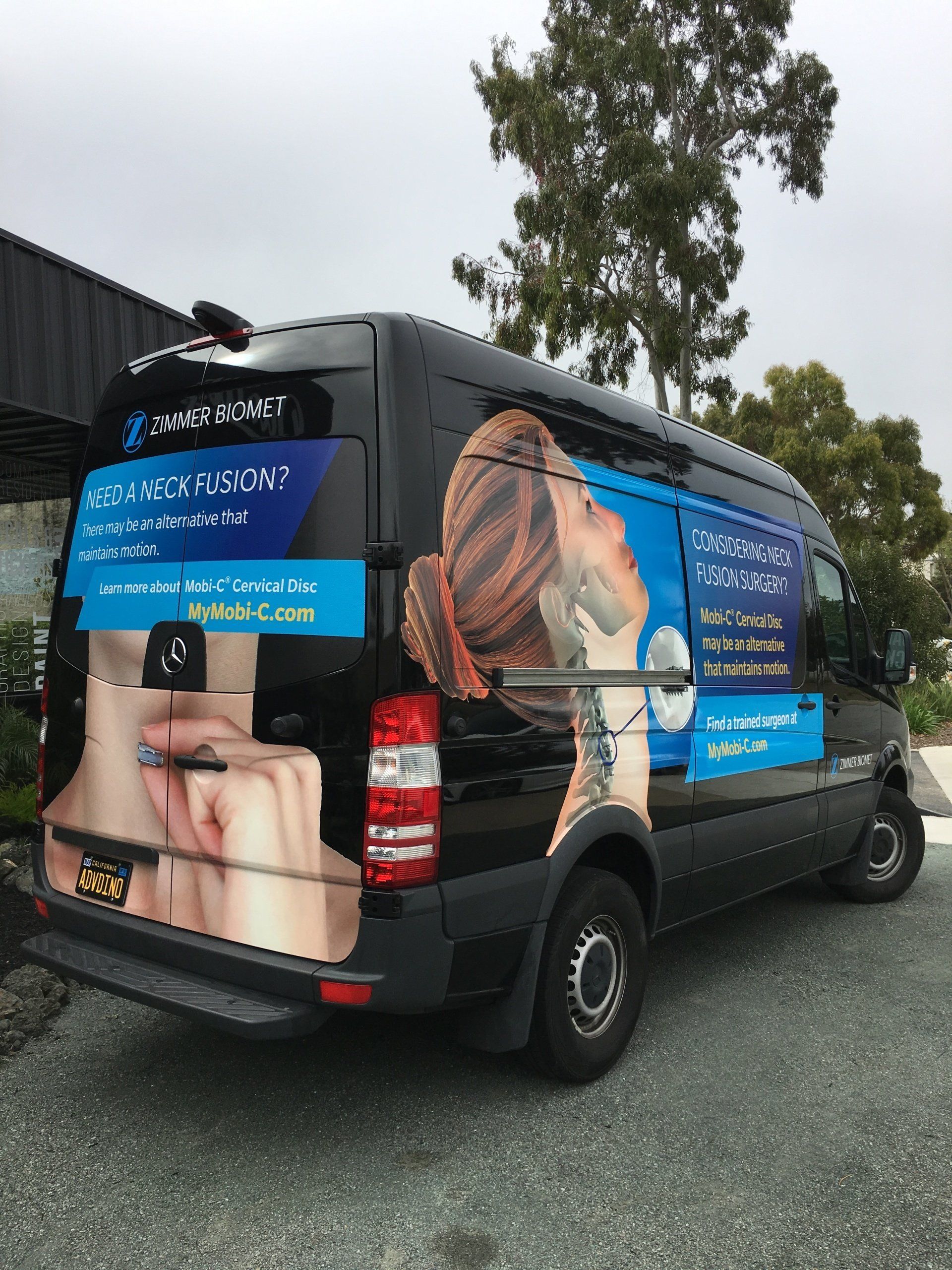 Wrapped black van with large blue-and-photo graphics parked outdoors on wet pavement