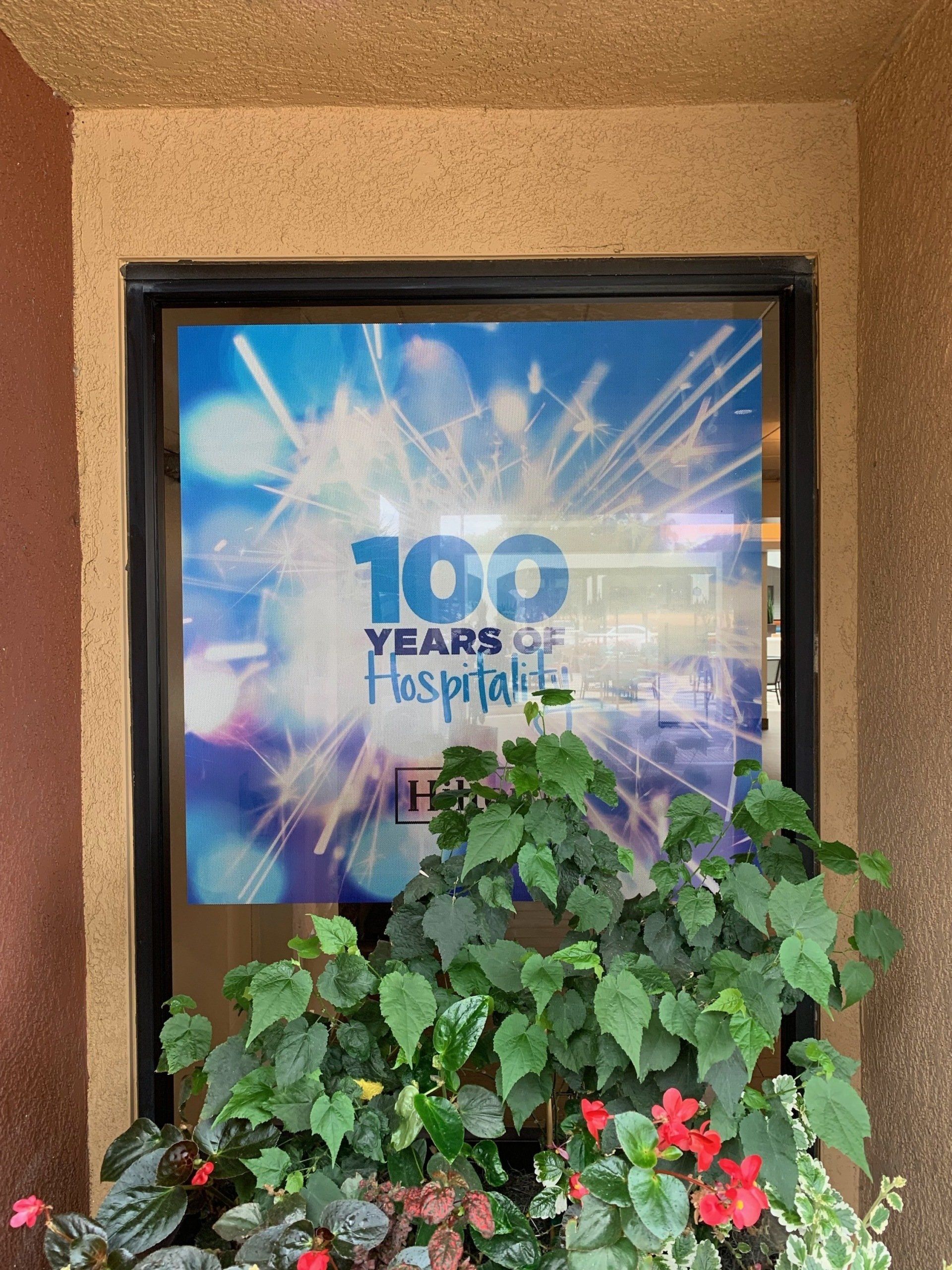 Poster reading “100 Years of Fashion” behind green and red plants against a tan wall