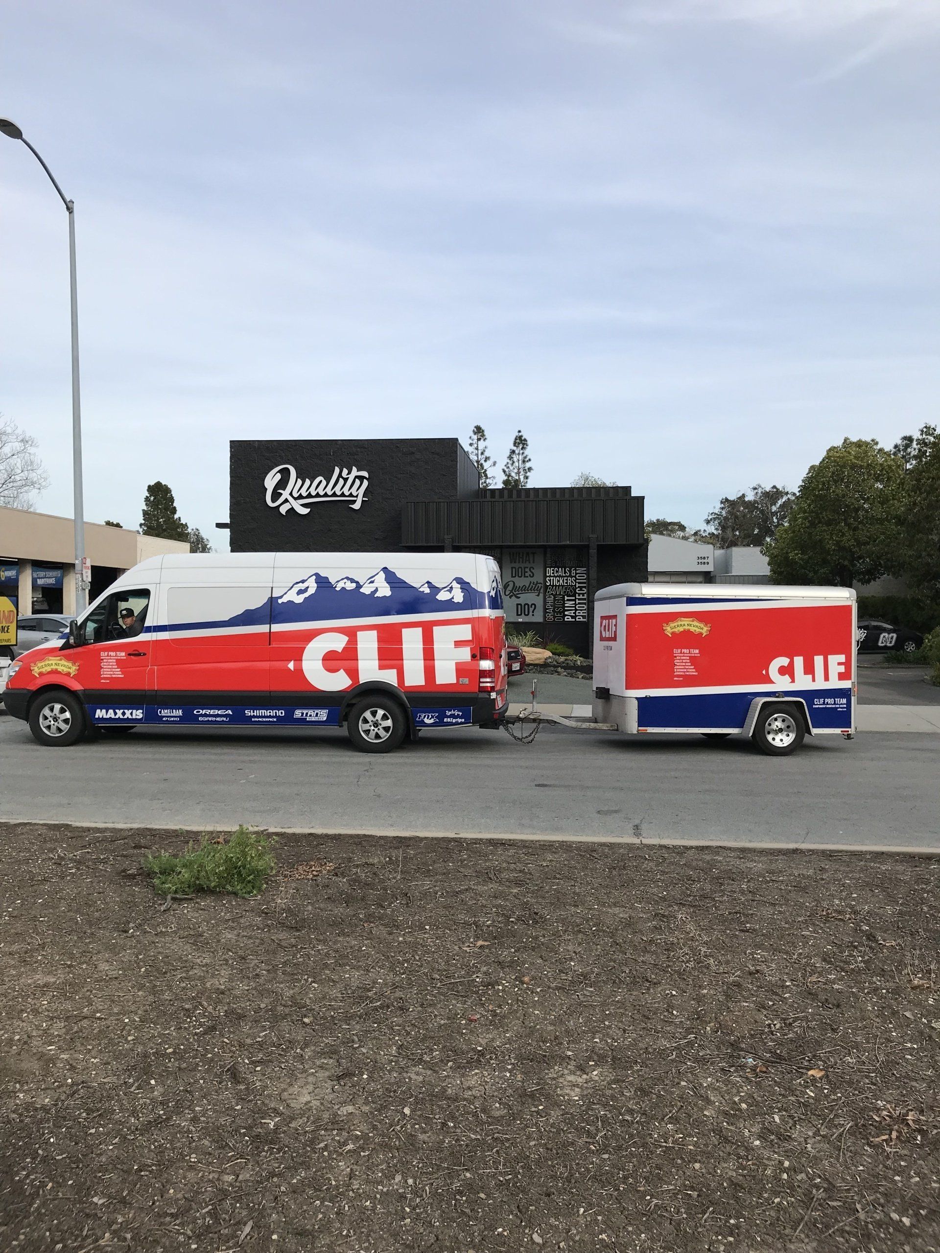 Red truck and trailer with large white lettering parked in a lot beside a black sign.