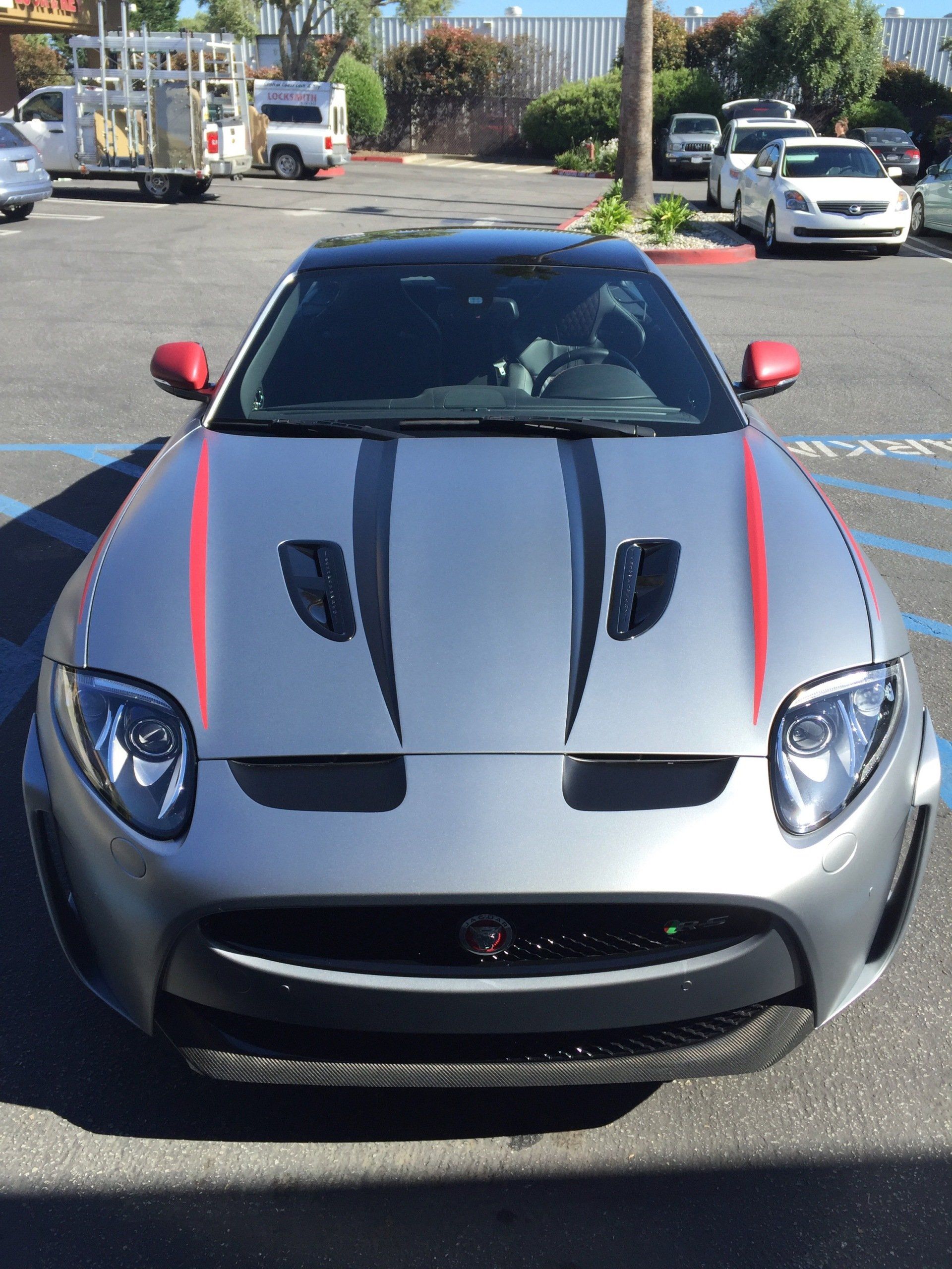 Front view of a silver sports car with black racing stripes and red mirrors parked outdoors