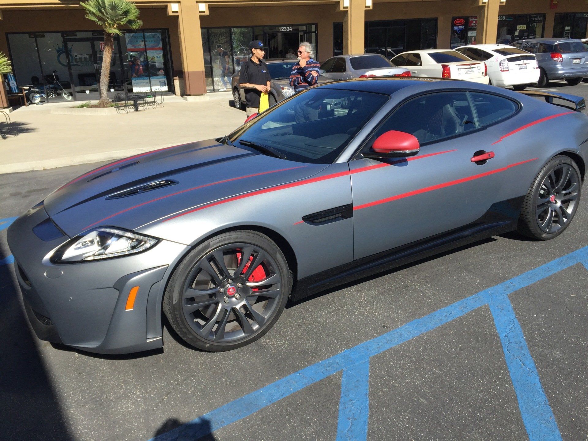 Gray sports coupe with red accents parked in a handicap space outside a storefront