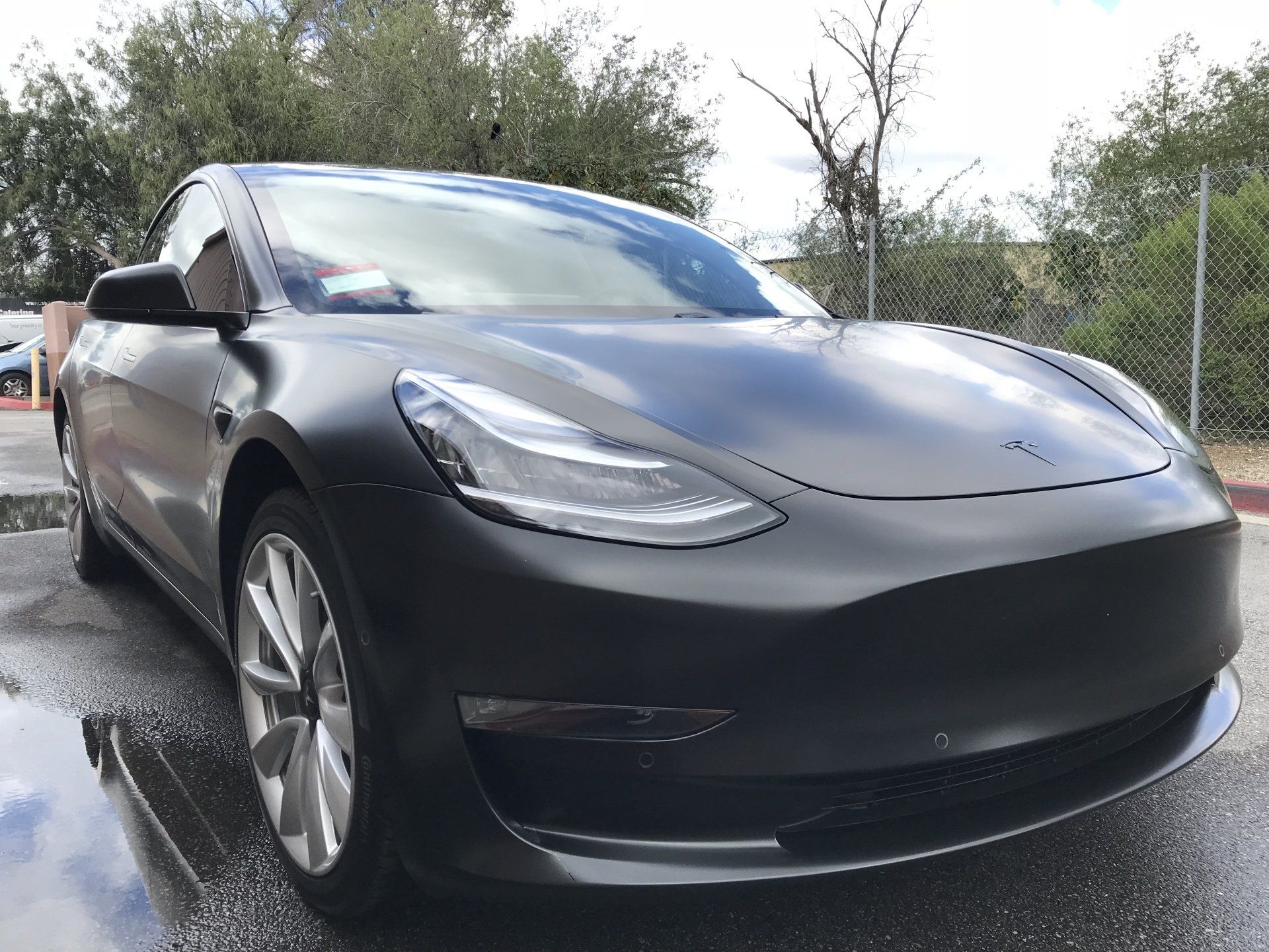 Matte black Tesla sedan parked on a wet road outdoors, front view