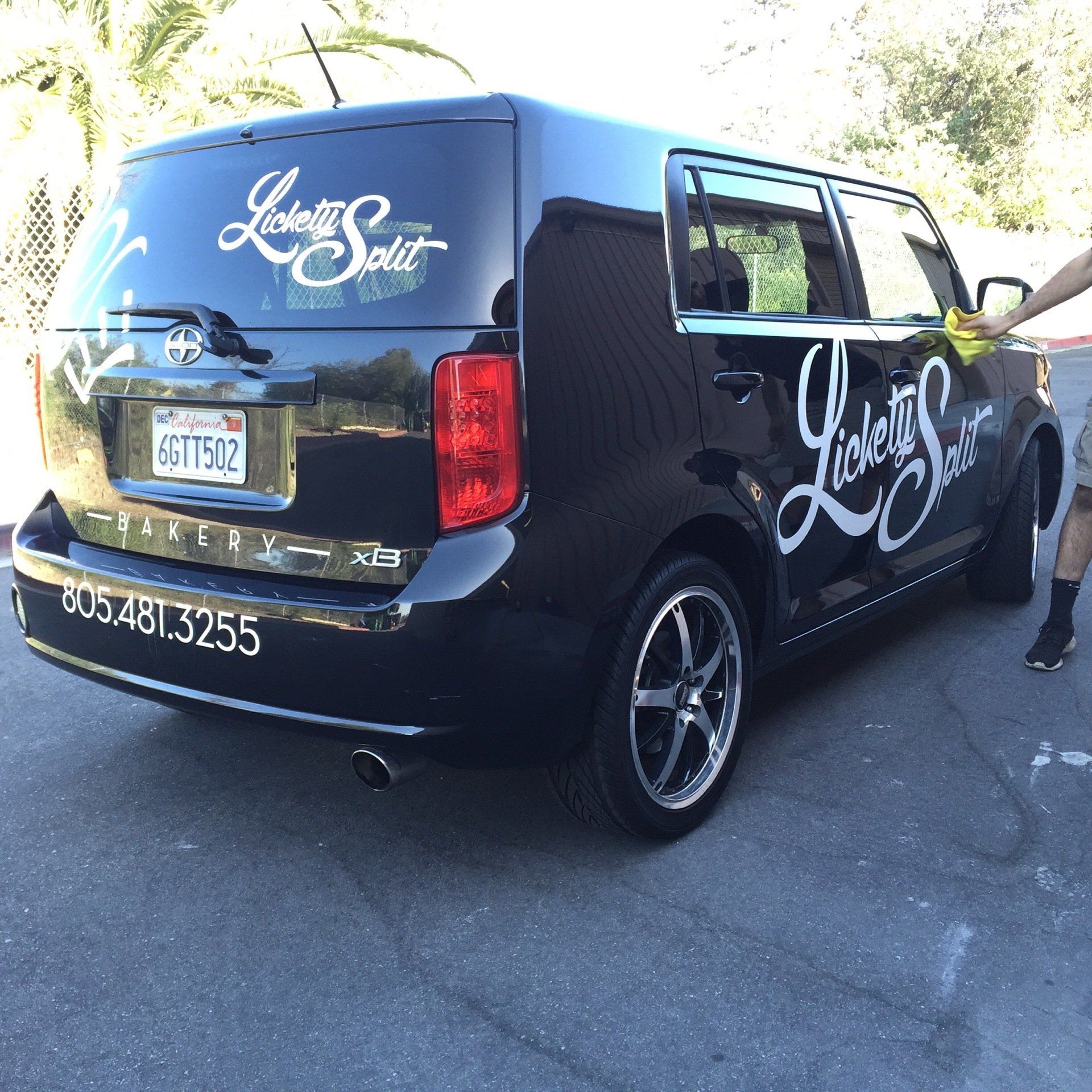 Black branded cargo van with chrome wheels parked outdoors, side door open and a person standing beside it