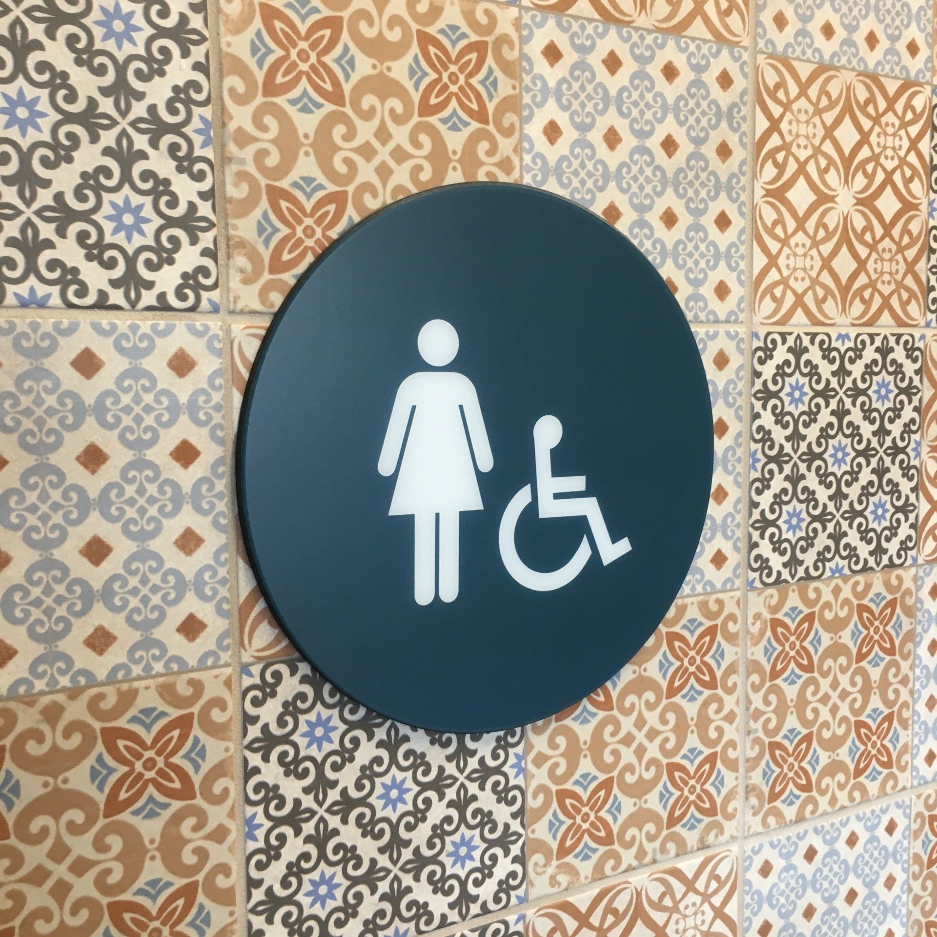 Accessible restroom sign with female and wheelchair symbols on patterned tile wall
