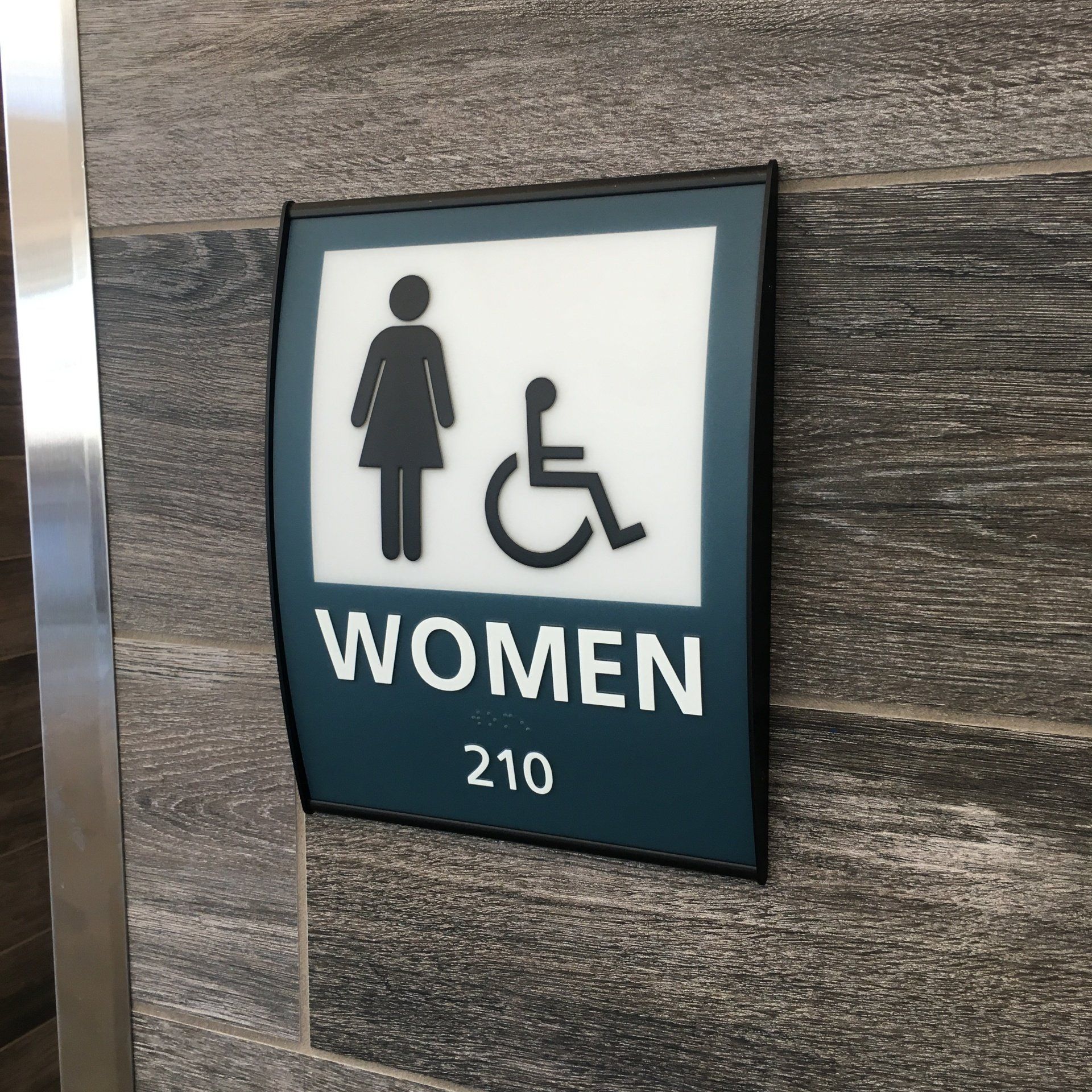 Women restroom sign with wheelchair accessibility symbol, room 210 on a wood-paneled wall