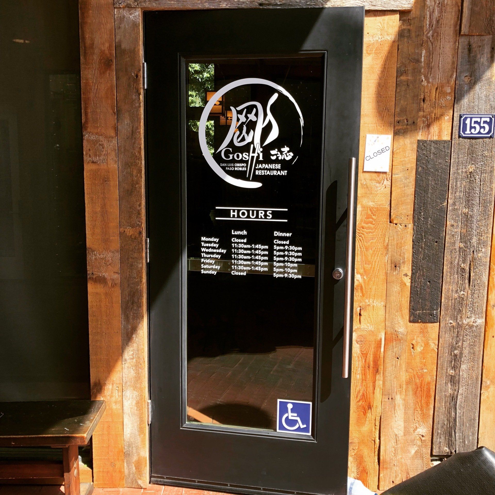 Black door with white “Cosi” sign and menu, set in a wooden storefront with accessibility symbol.
