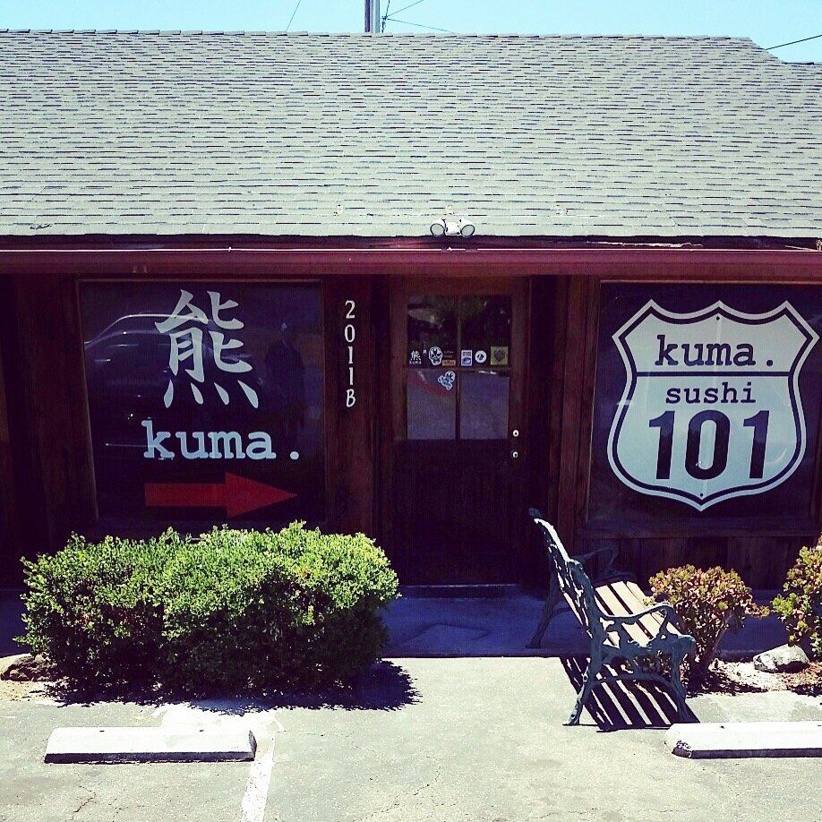 Front of Kuma Sushi 101 with Japanese signage, dark red facade, and a small shrub in front