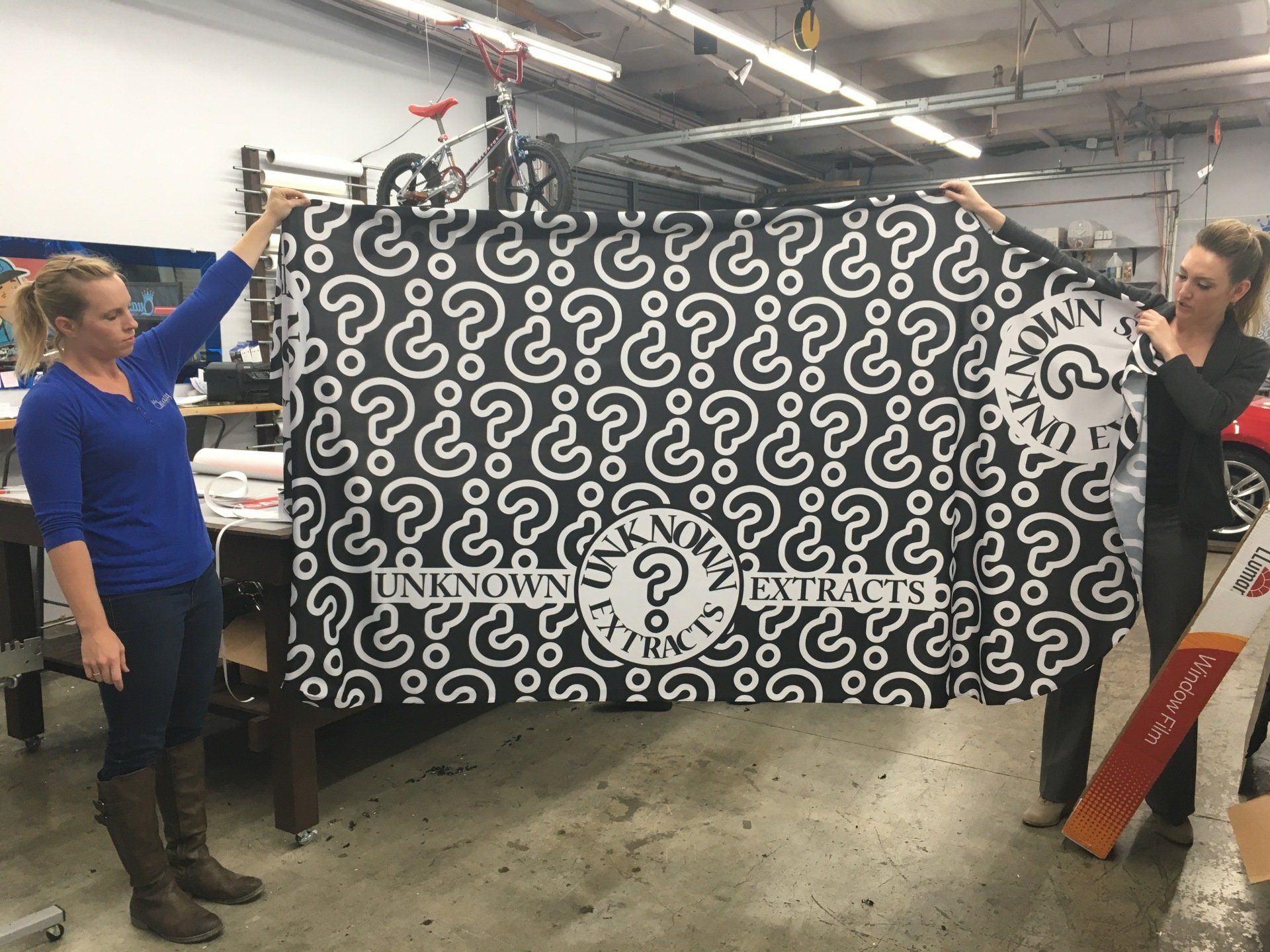 Two people hold a large black-and-white patterned fabric banner in a workshop.