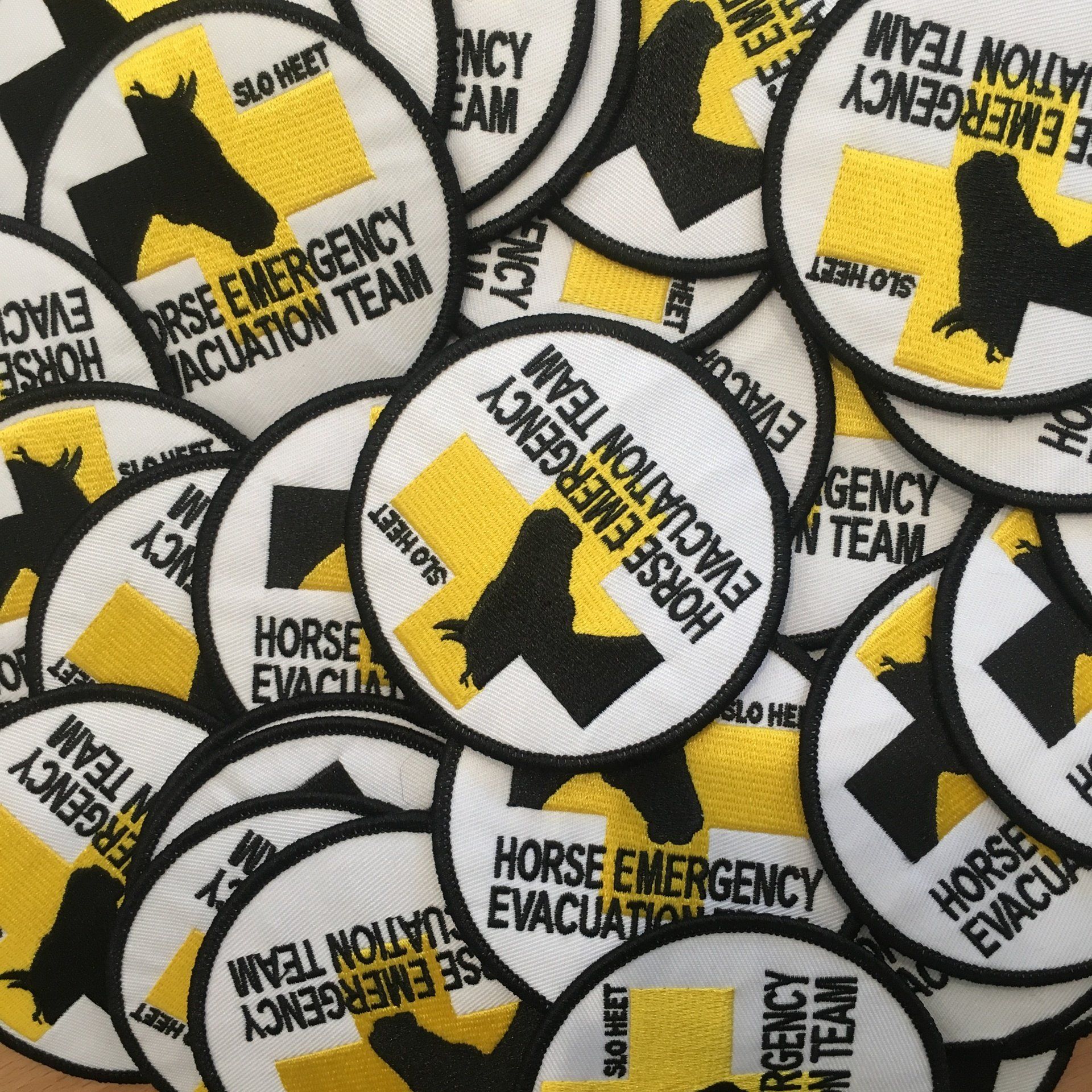 Close-up of yellow and black “Horse Emergency Evacuation Team” patches scattered together