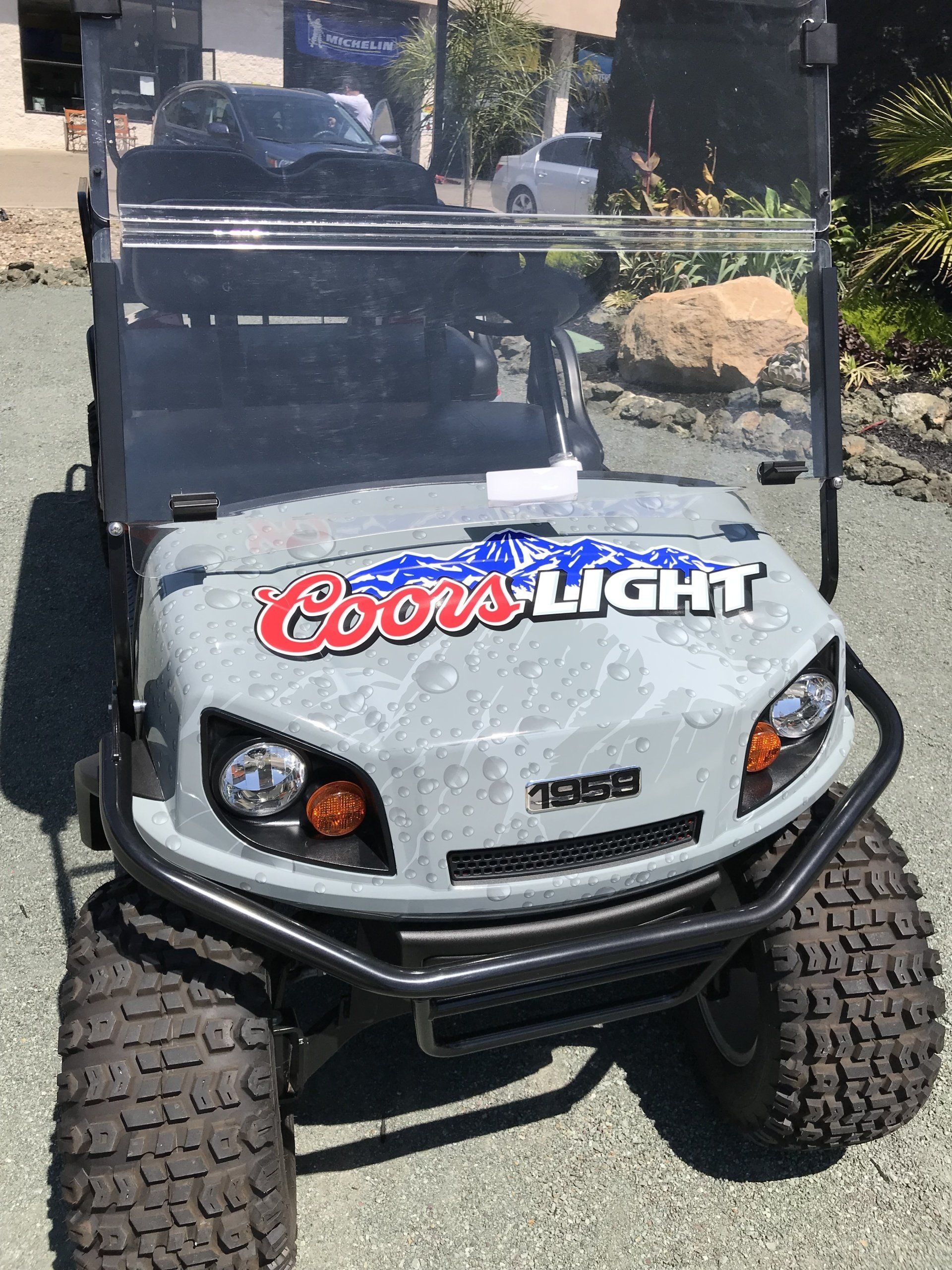 Gray off-road golf cart with Coors Light logo, large tires, and black roll cage on a driveway