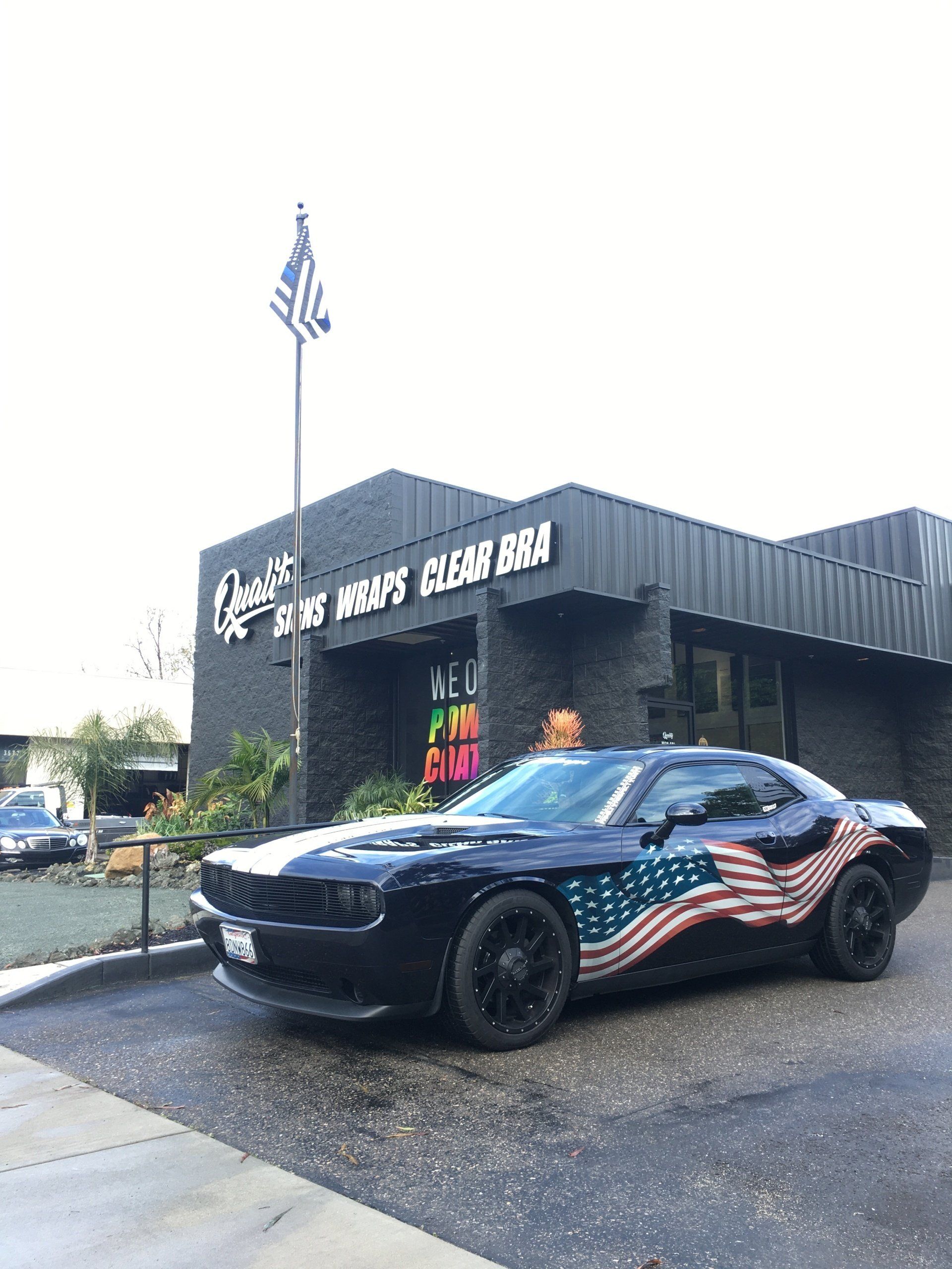 Black sports car with American flag wrap parked outside a building with a flagpole.