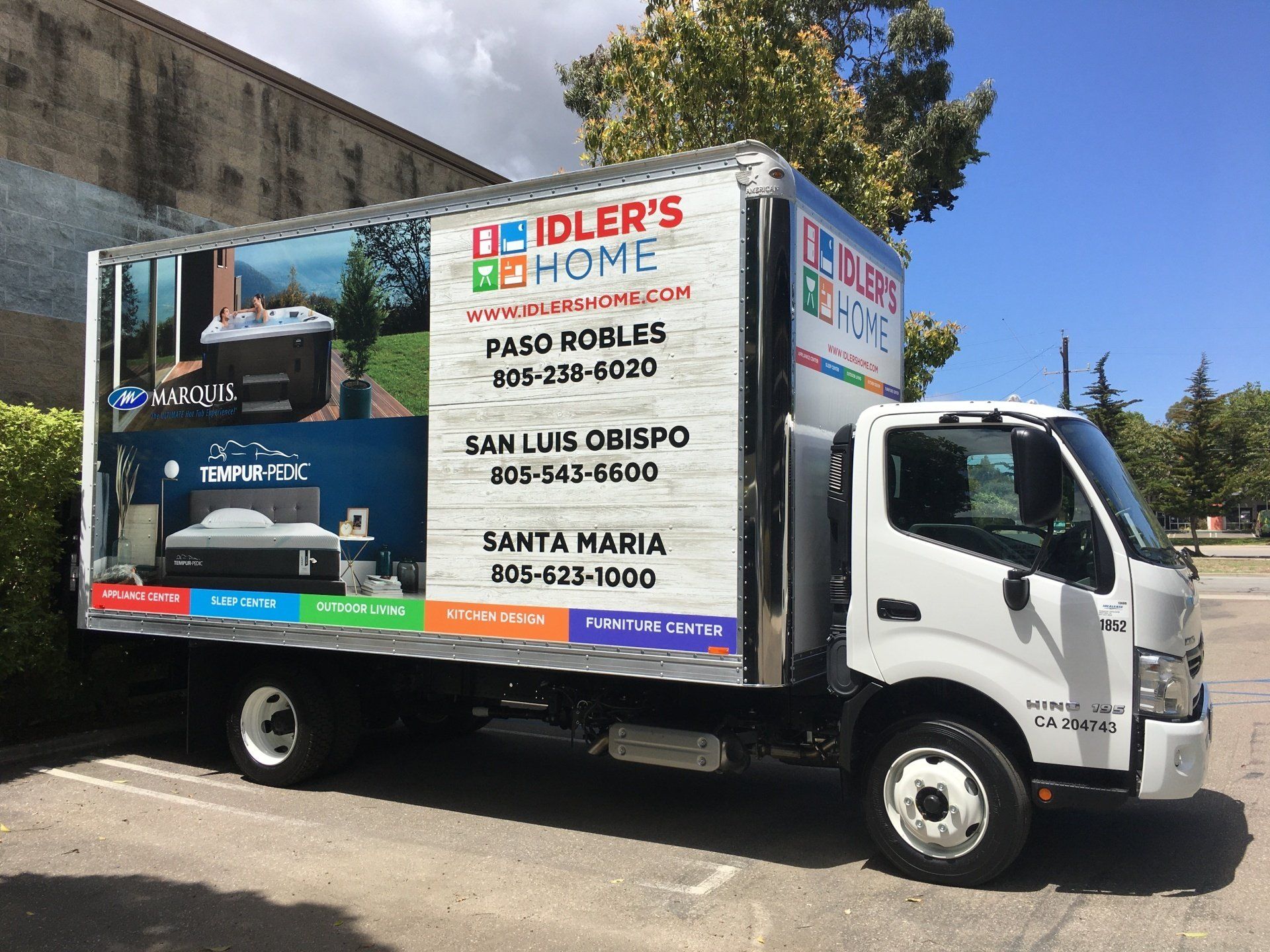 White box truck with colorful business advertising parked on a street in front of a wall.