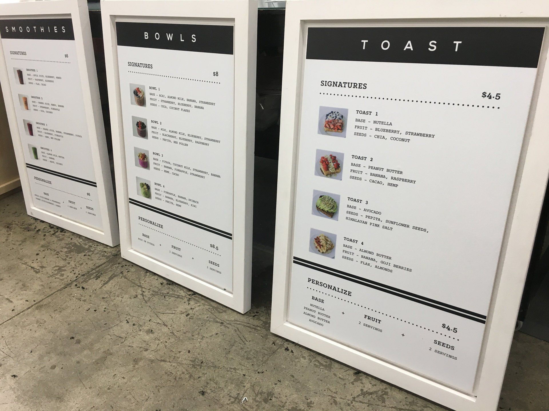 Three framed menu boards with black headers stand on a tiled floor indoors.