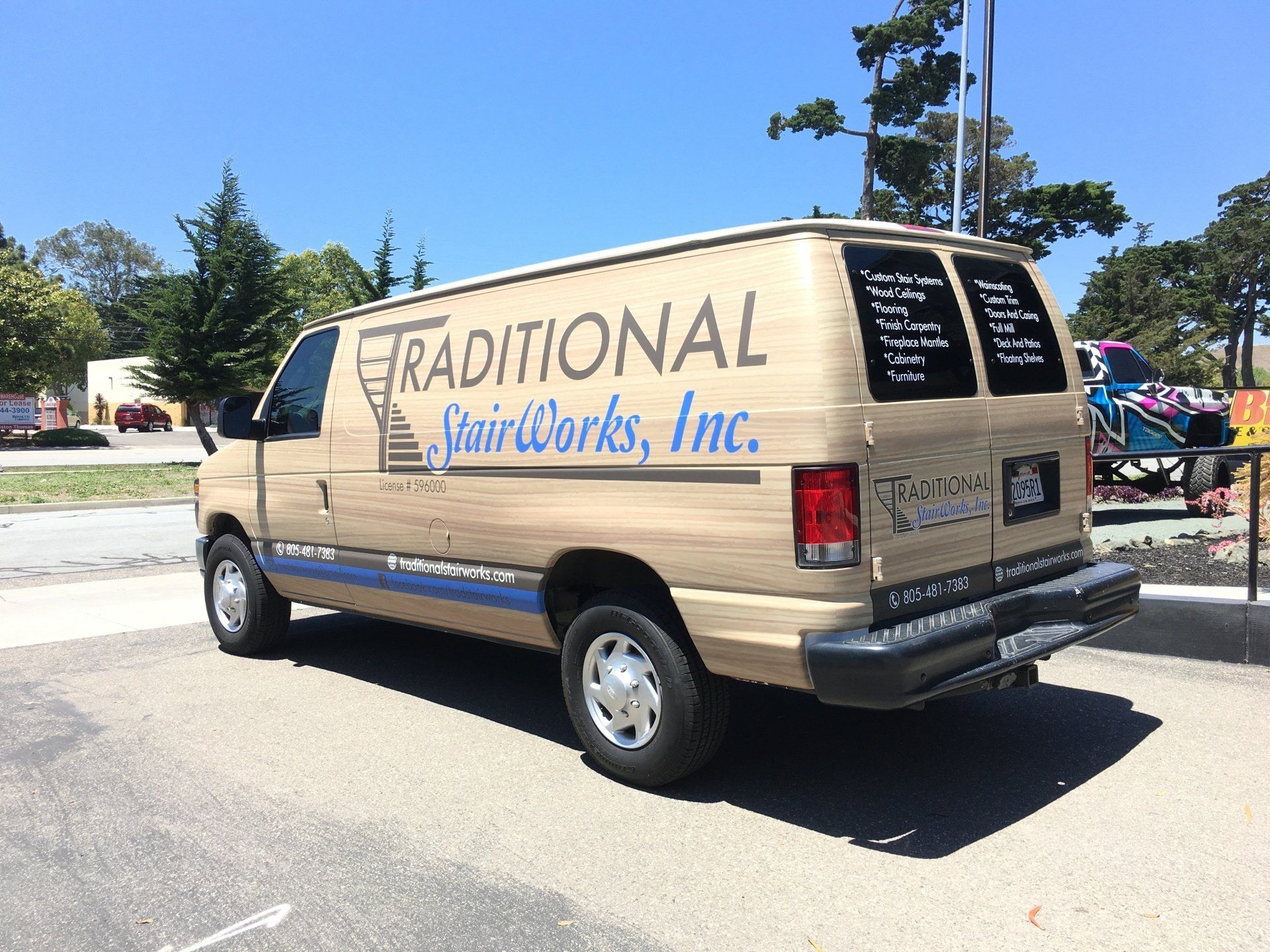Tan van with “Traditional Hairworks, Inc.” signage parked outdoors near trees and tents