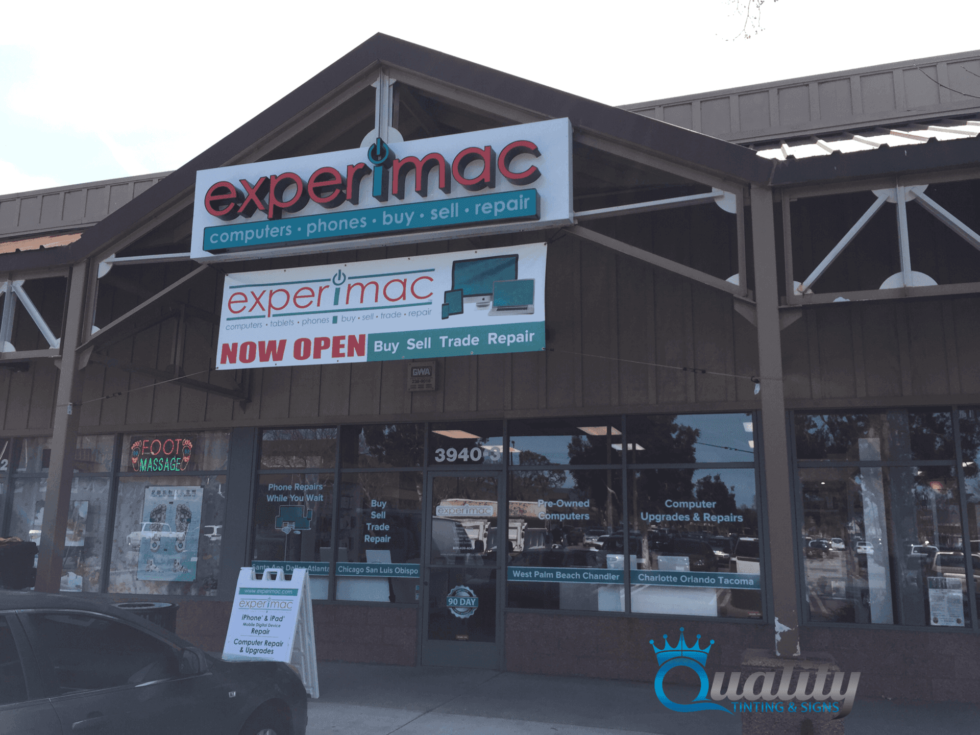 Experimac storefront with signs and open door in a strip mall storefront