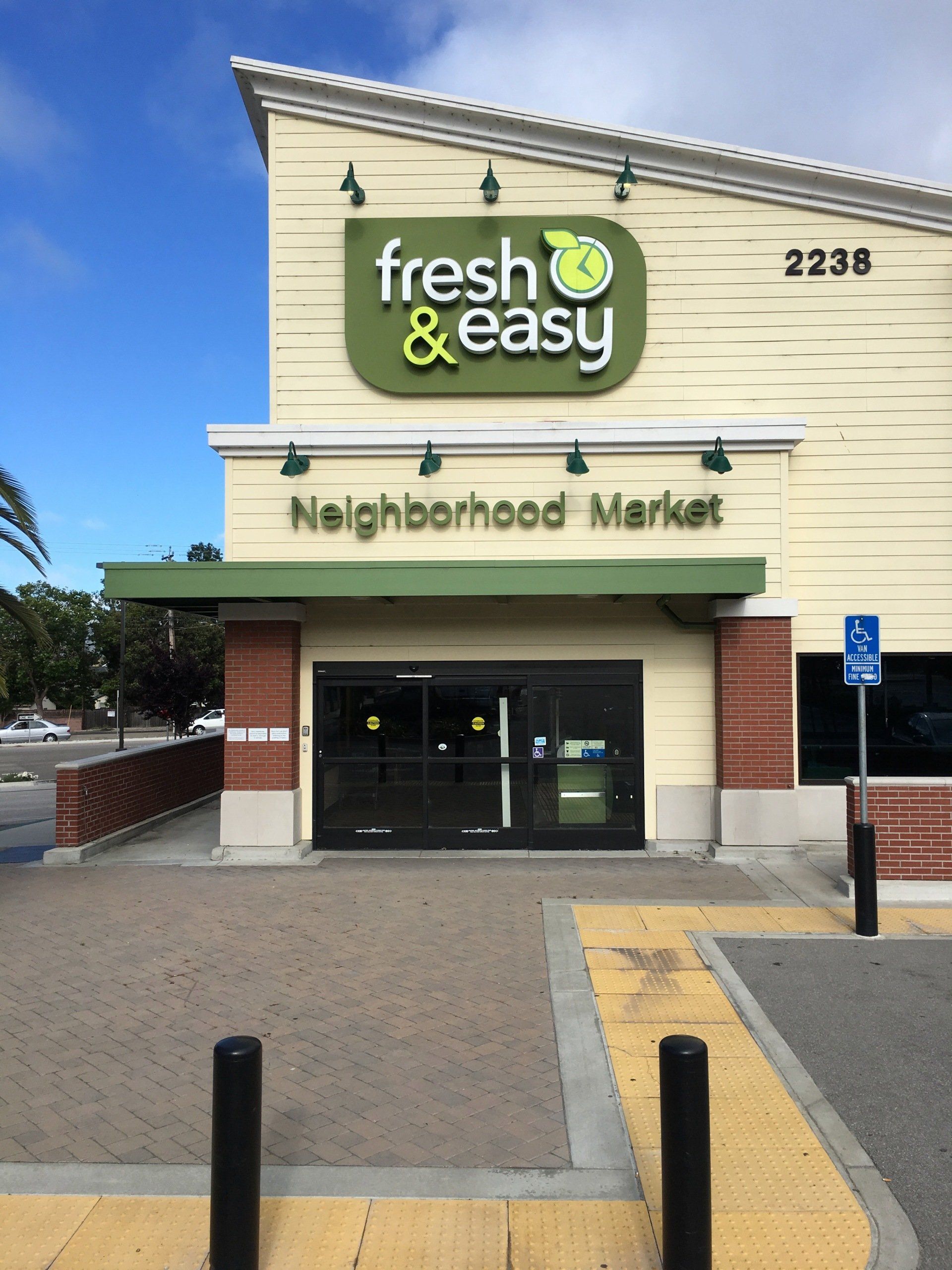 Fresh & Easy Neighborhood Market storefront with green sign and glass entrance under a blue sky