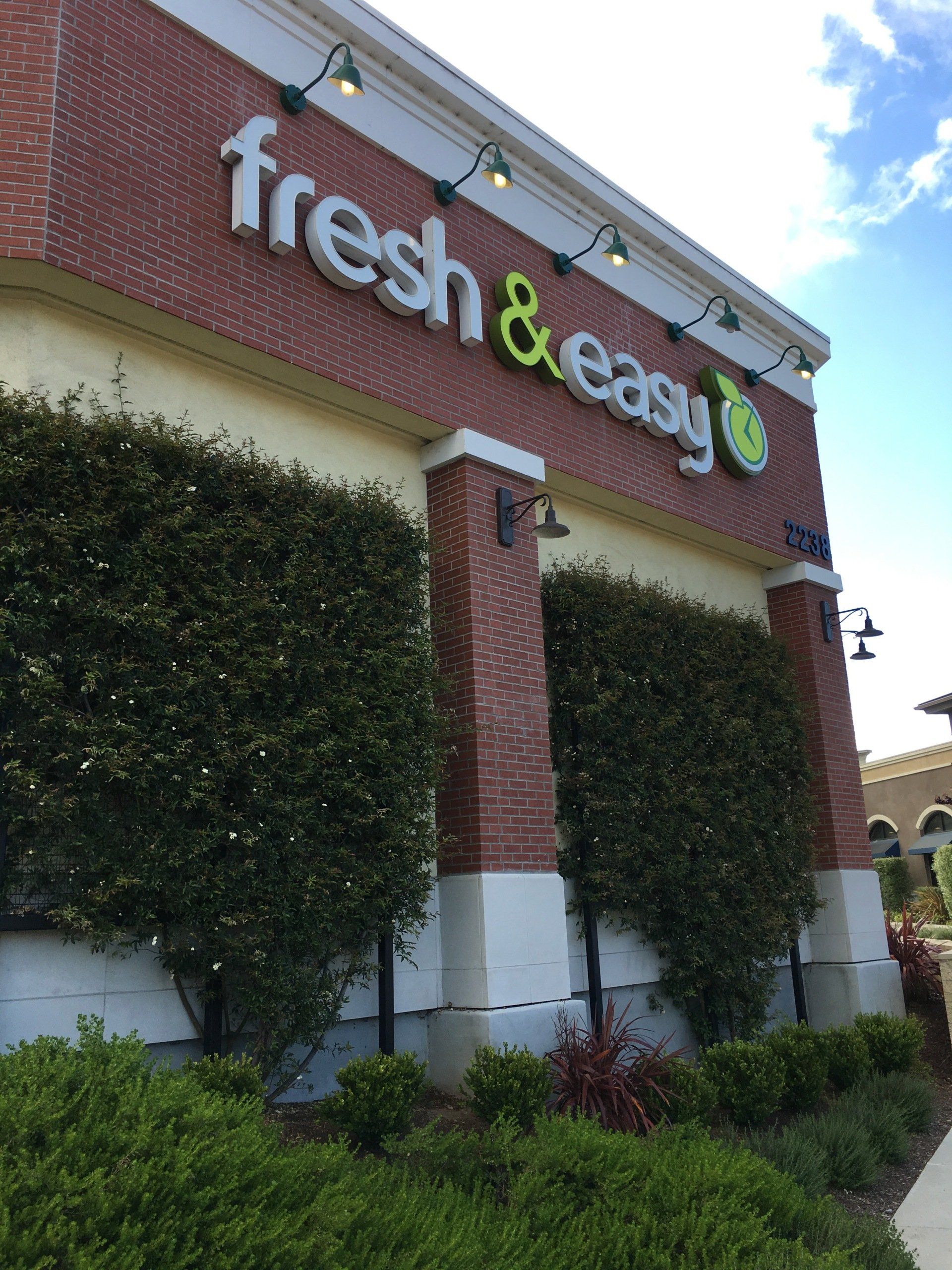 Fresh & Easy store sign on a brick building with green landscaping below.