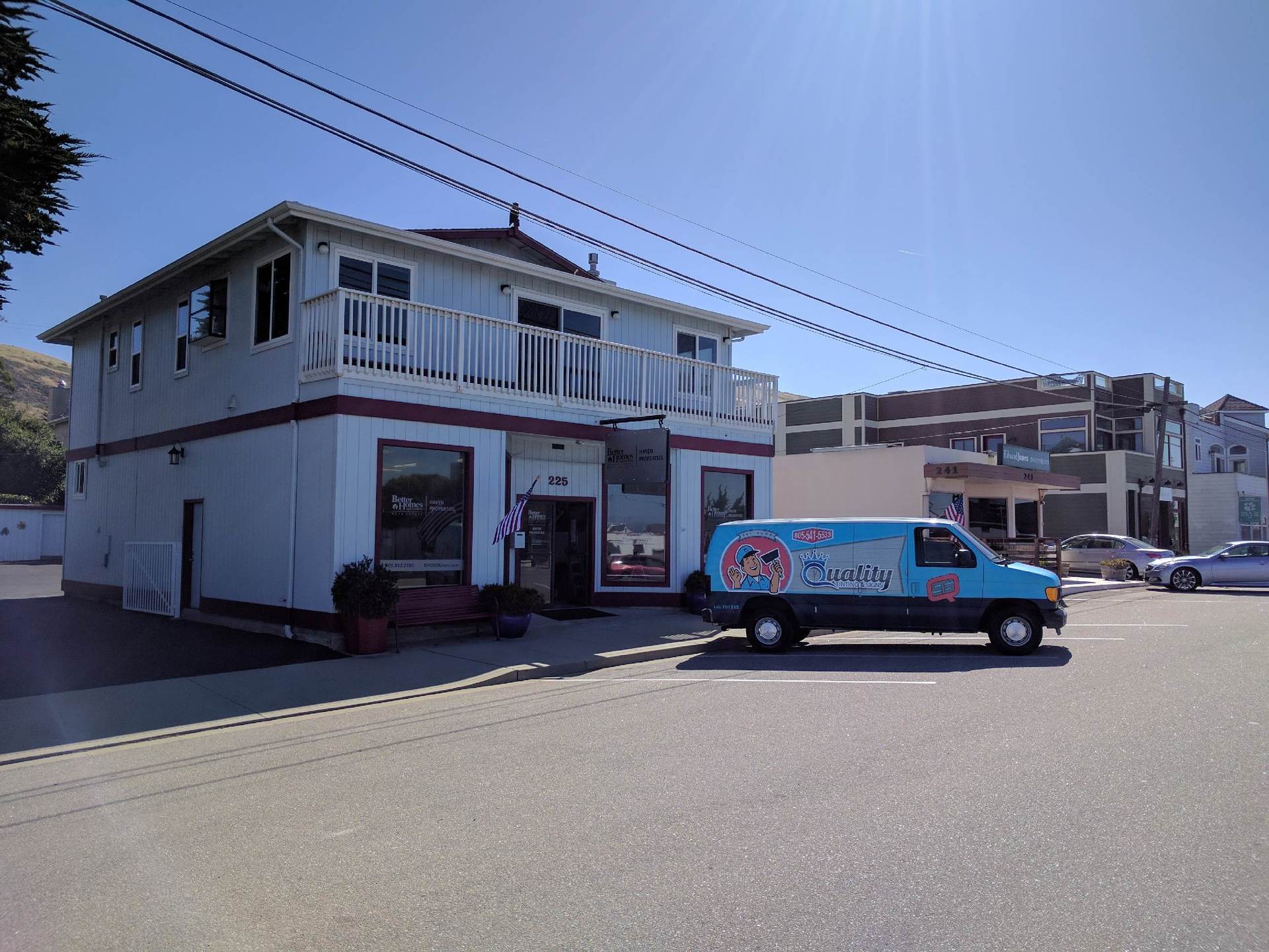 Blue service van parked beside a white two-story building on a sunny street.