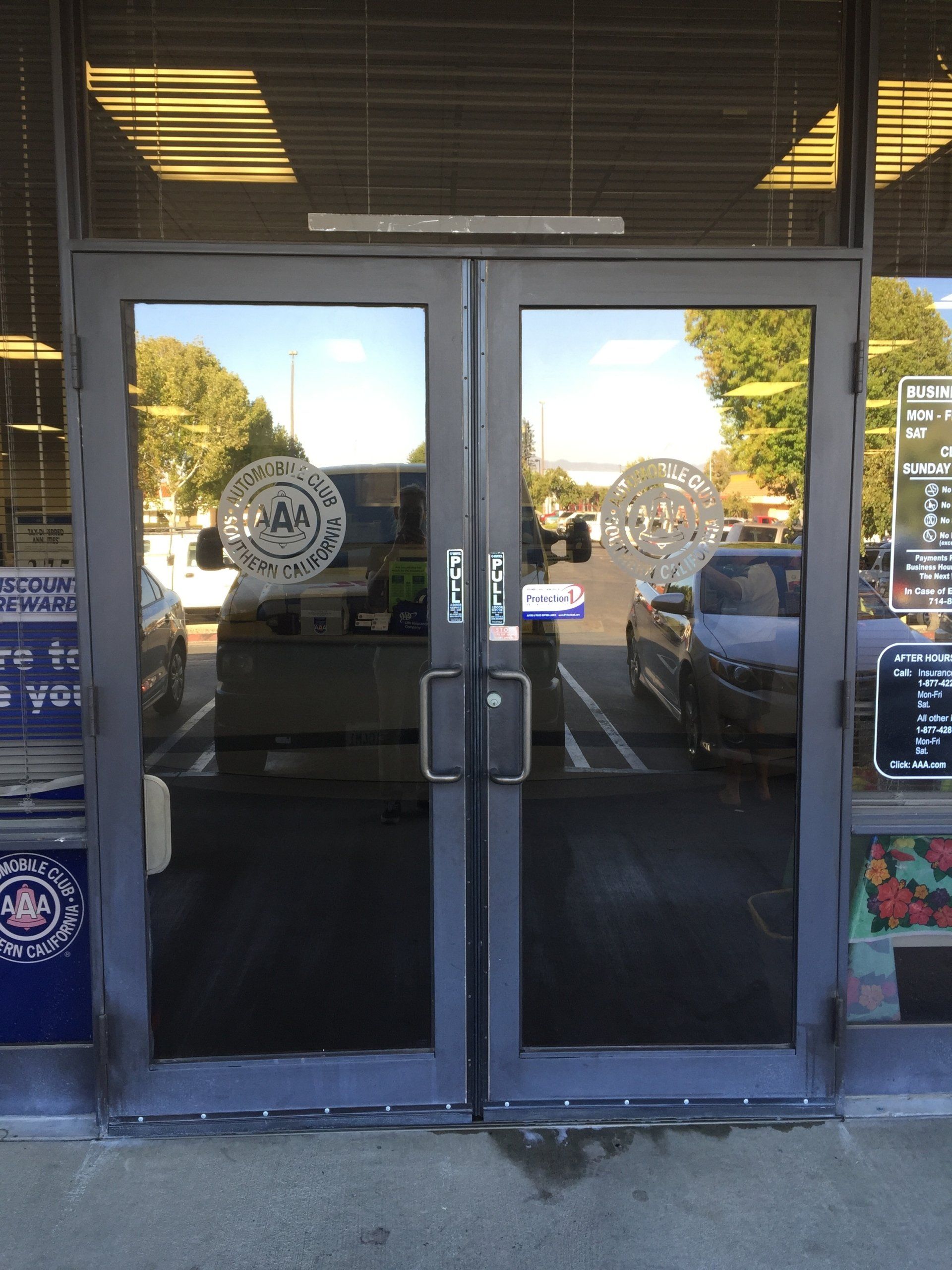 Glass storefront entrance with double doors, reflections, and signs in the windows