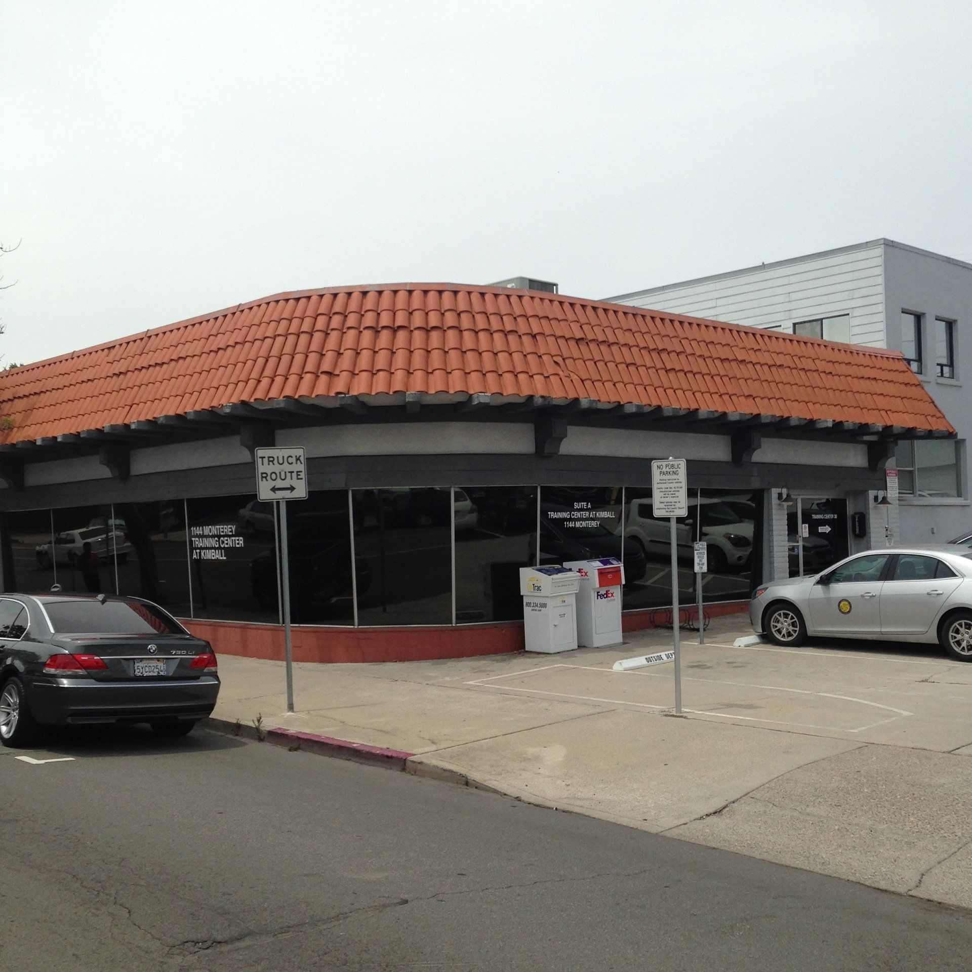 Corner storefront with orange tile roof, large windows, and parked cars in front on a street.