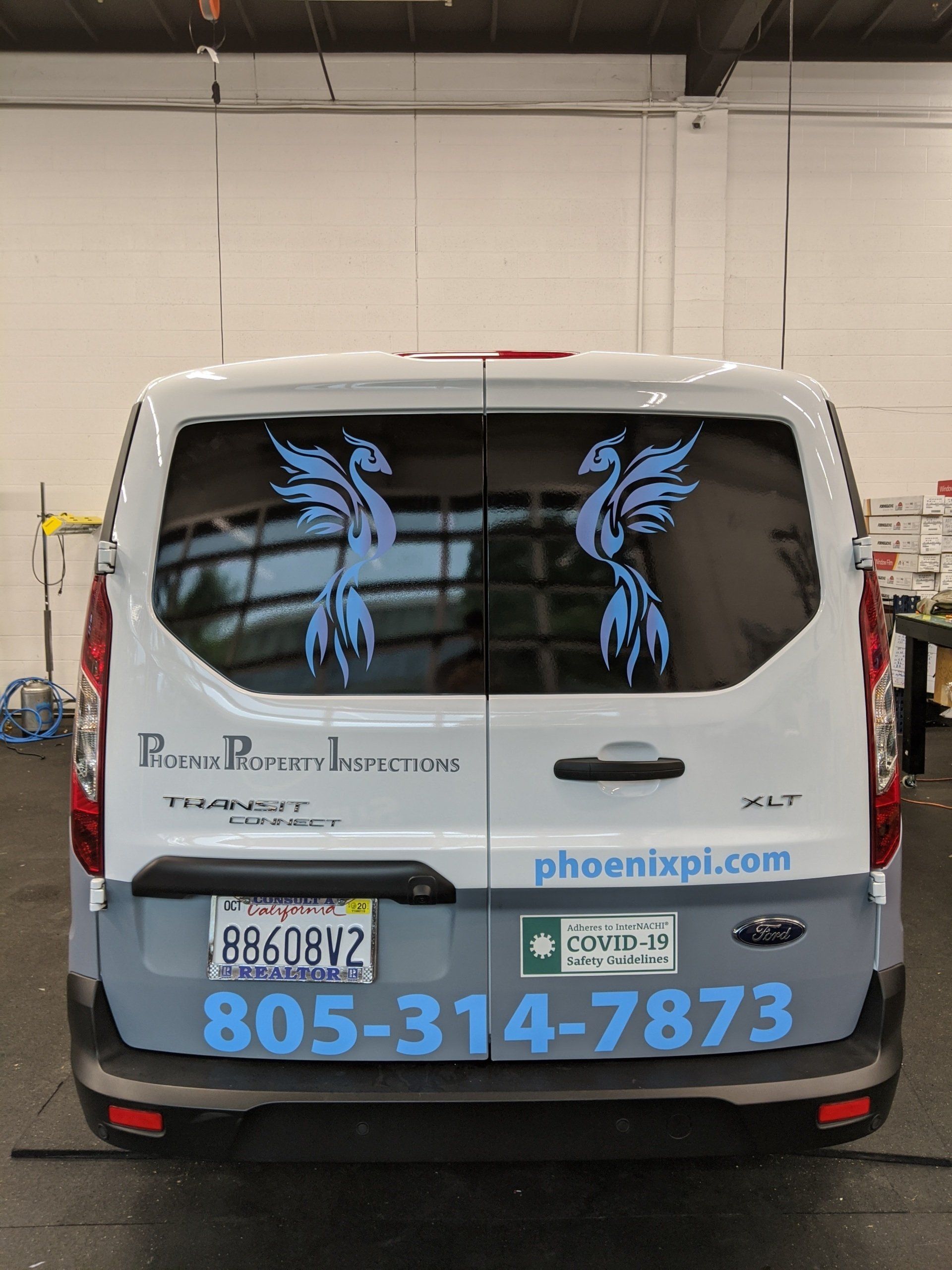 White service van rear with blue phoenix decals and large phone number inside a garage.