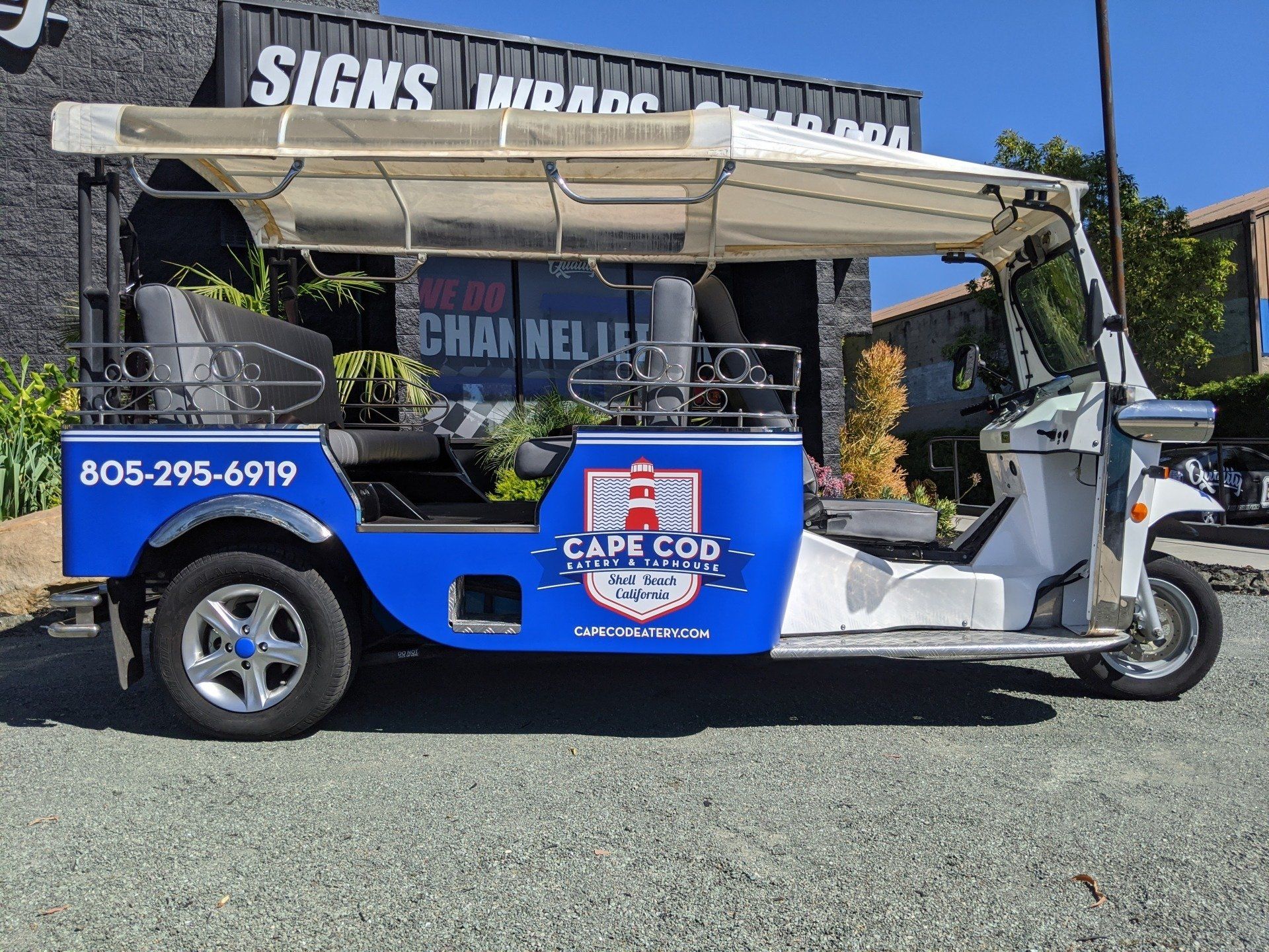Blue and white open-air shuttle cart parked outdoors with a canopy and company logo on the side.