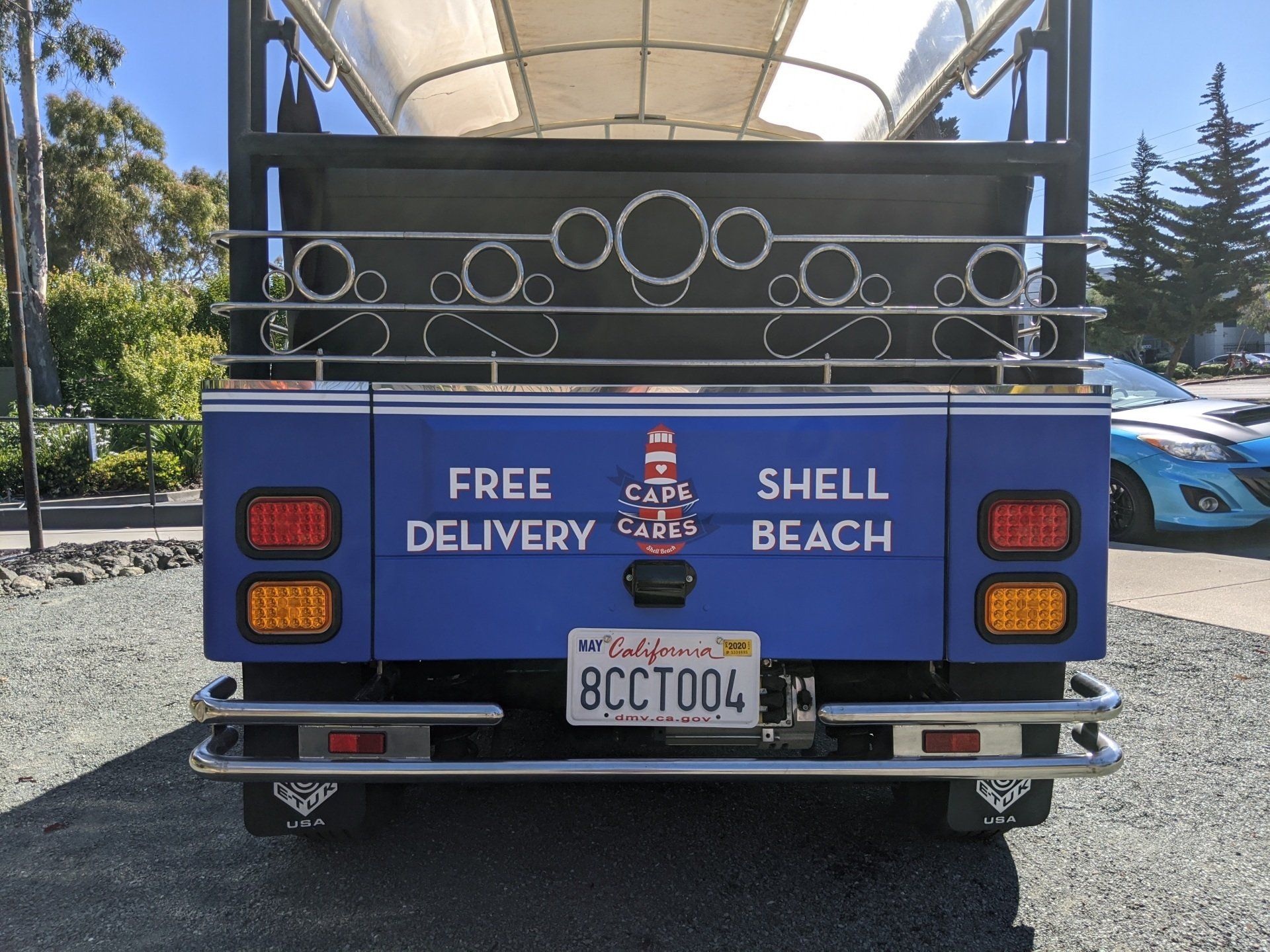 Blue truck rear with “Free Delivery” and “Shell Beach” text, parked outdoors with a tank behind it.