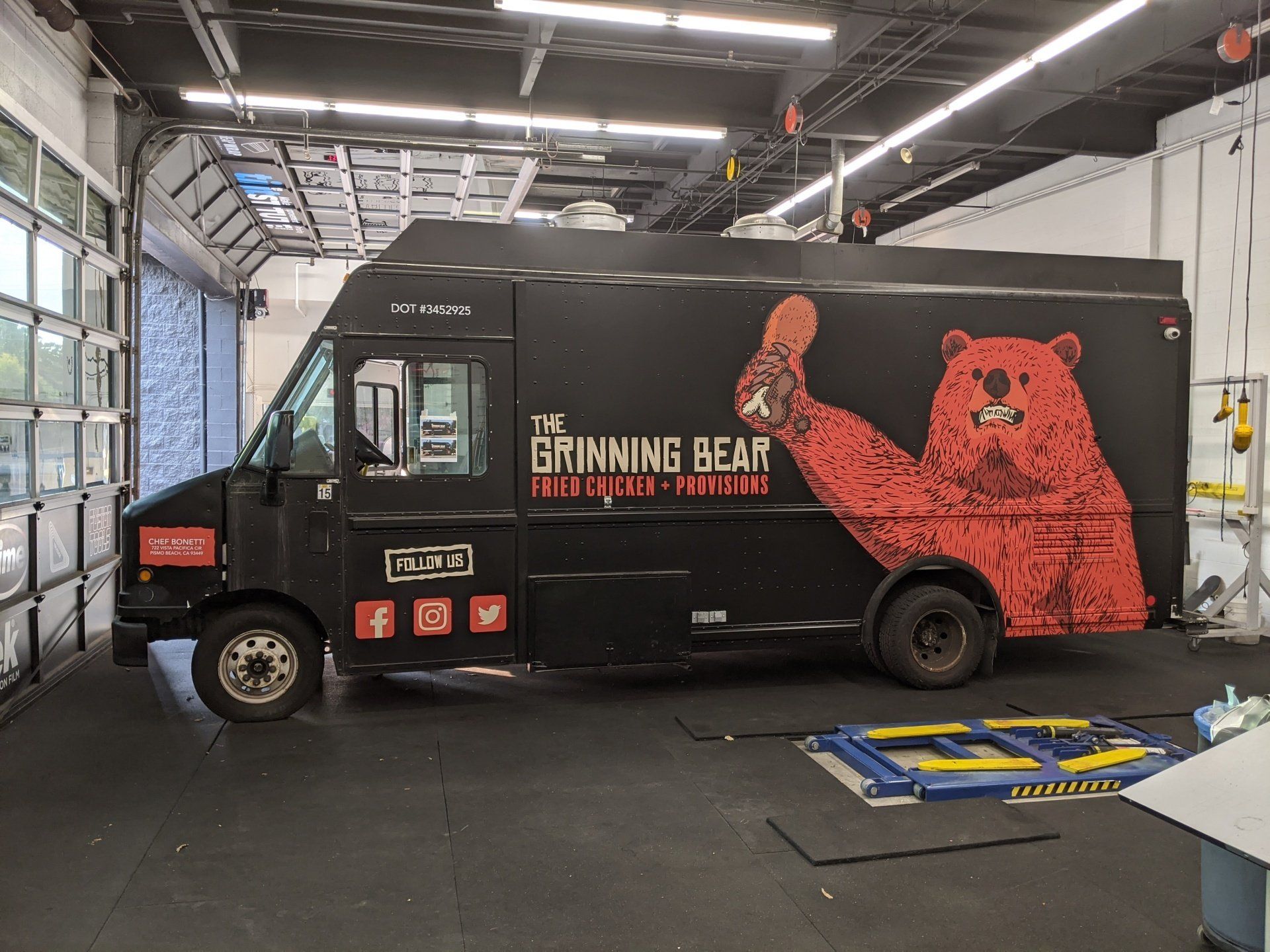 Black food truck in a garage, branded “The Grinning Bear” with a large red bear graphic.