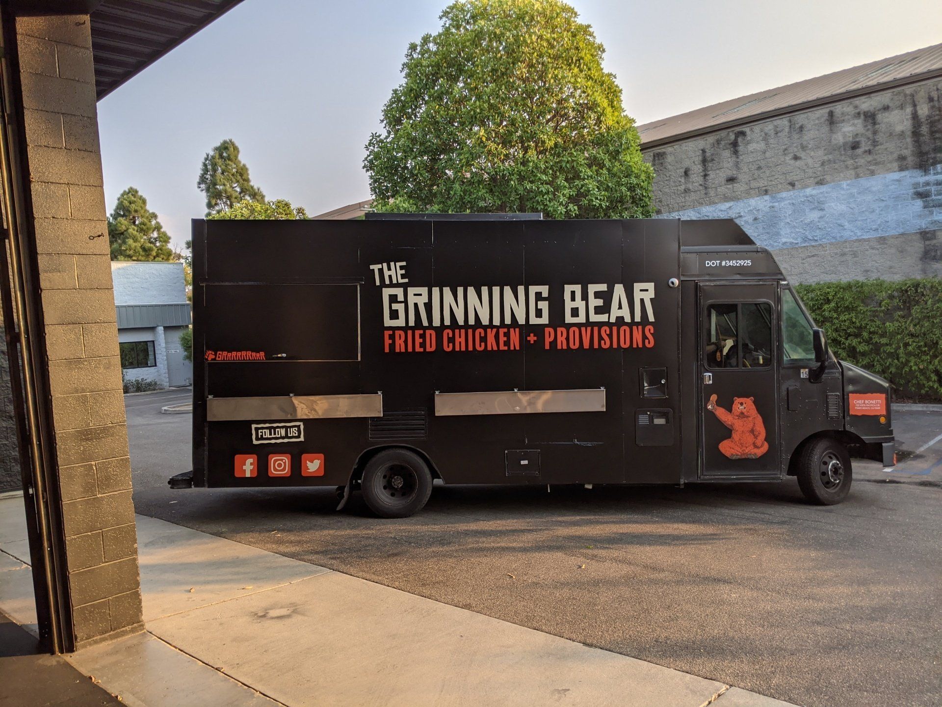 Black food truck reading “The Grinding Bear” parked in a lot beside a building