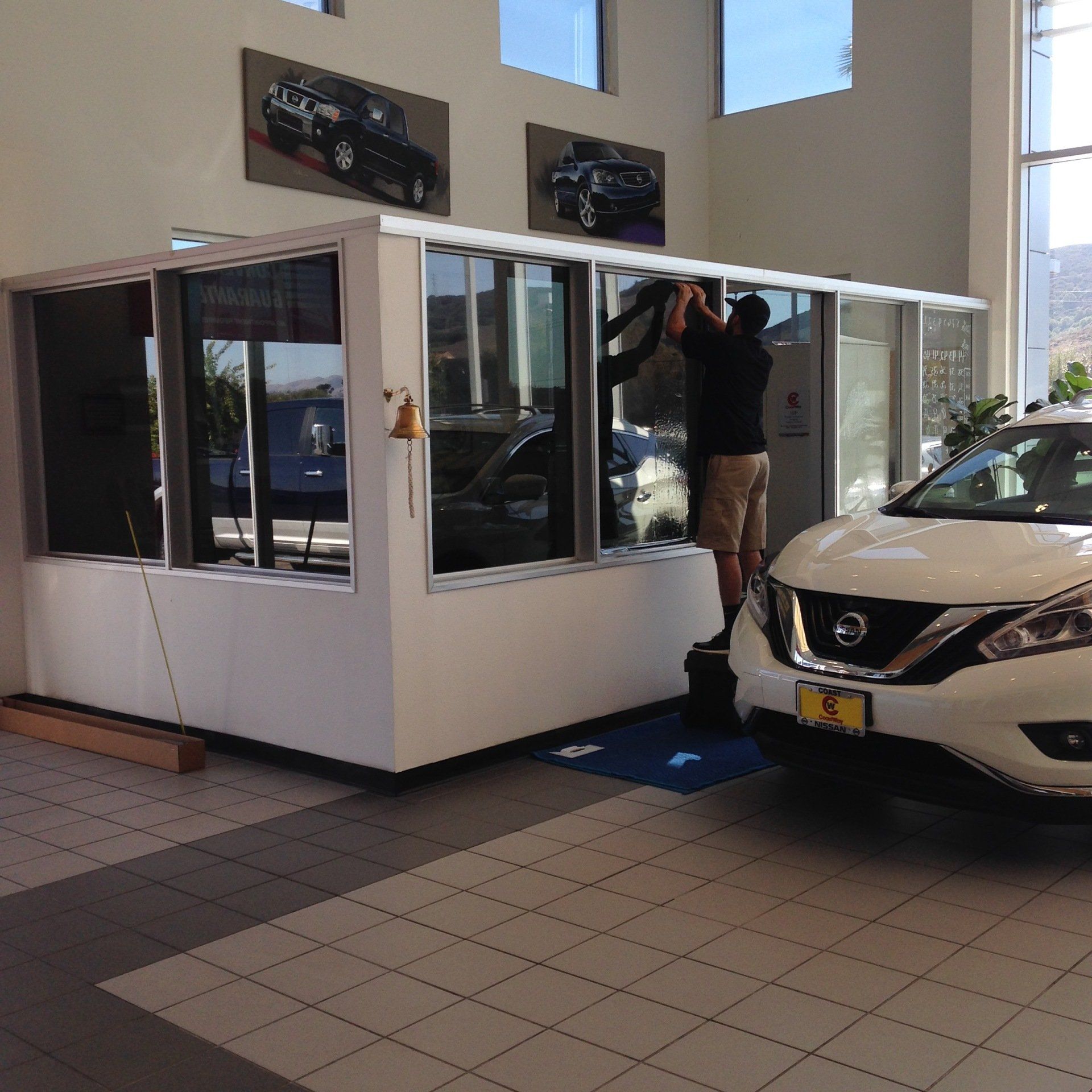 Car showroom with a person working on a white display booth beside a parked white Nissan SUV