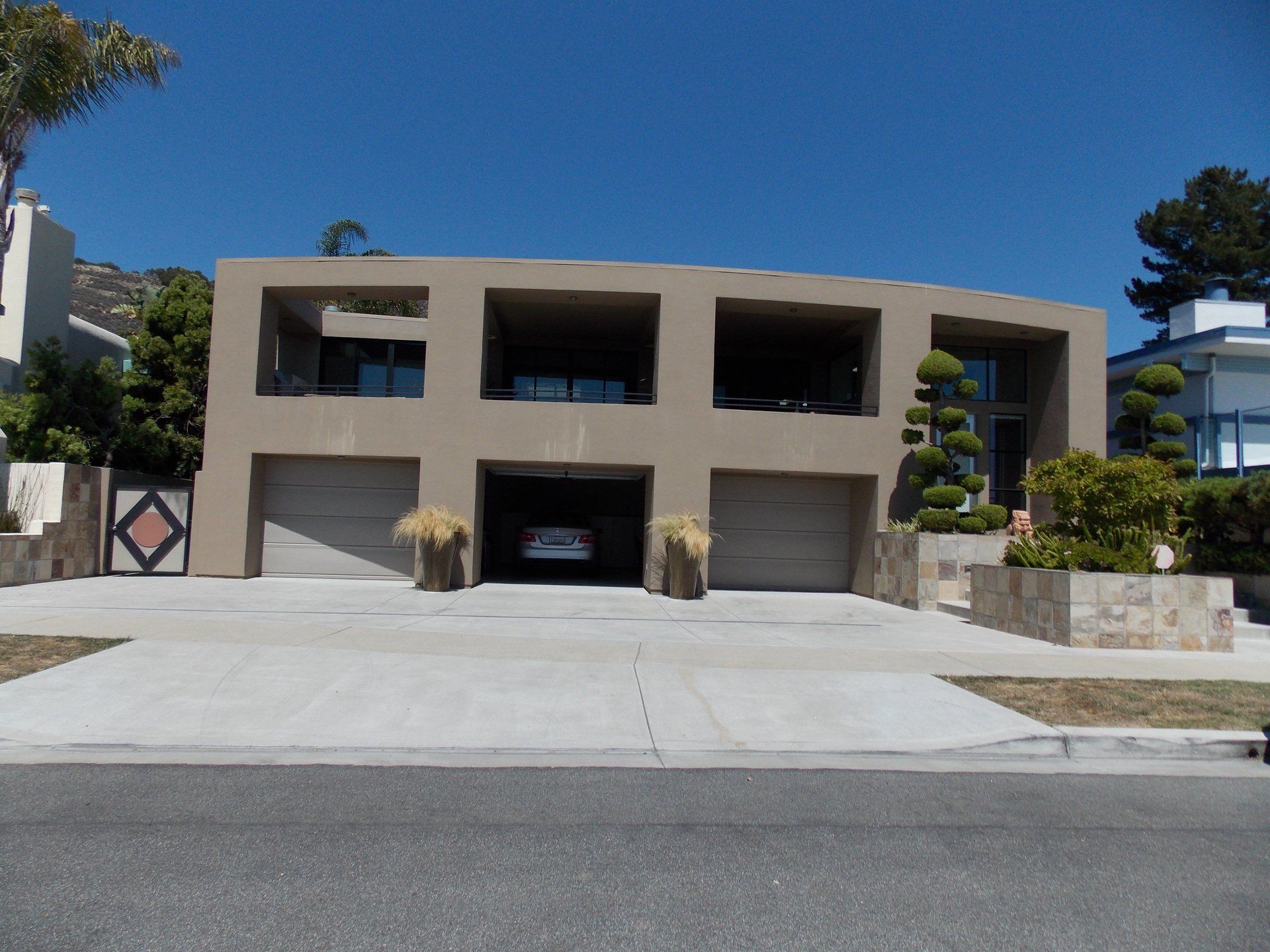 Modern two-story house with a wide driveway, three garage doors, and desert landscaping under a clear blue sky