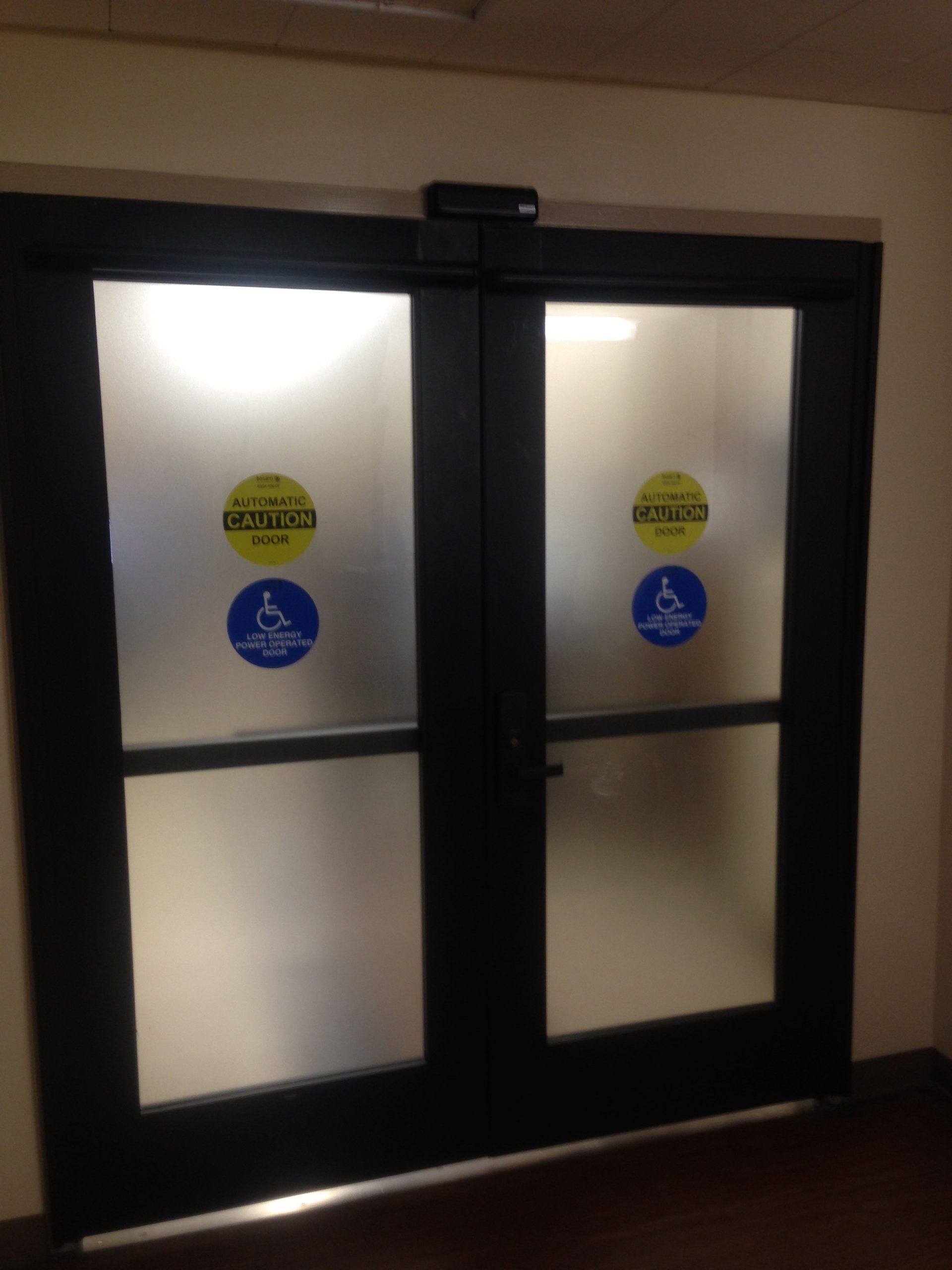 Black-framed frosted glass double doors with safety decals at an entrance