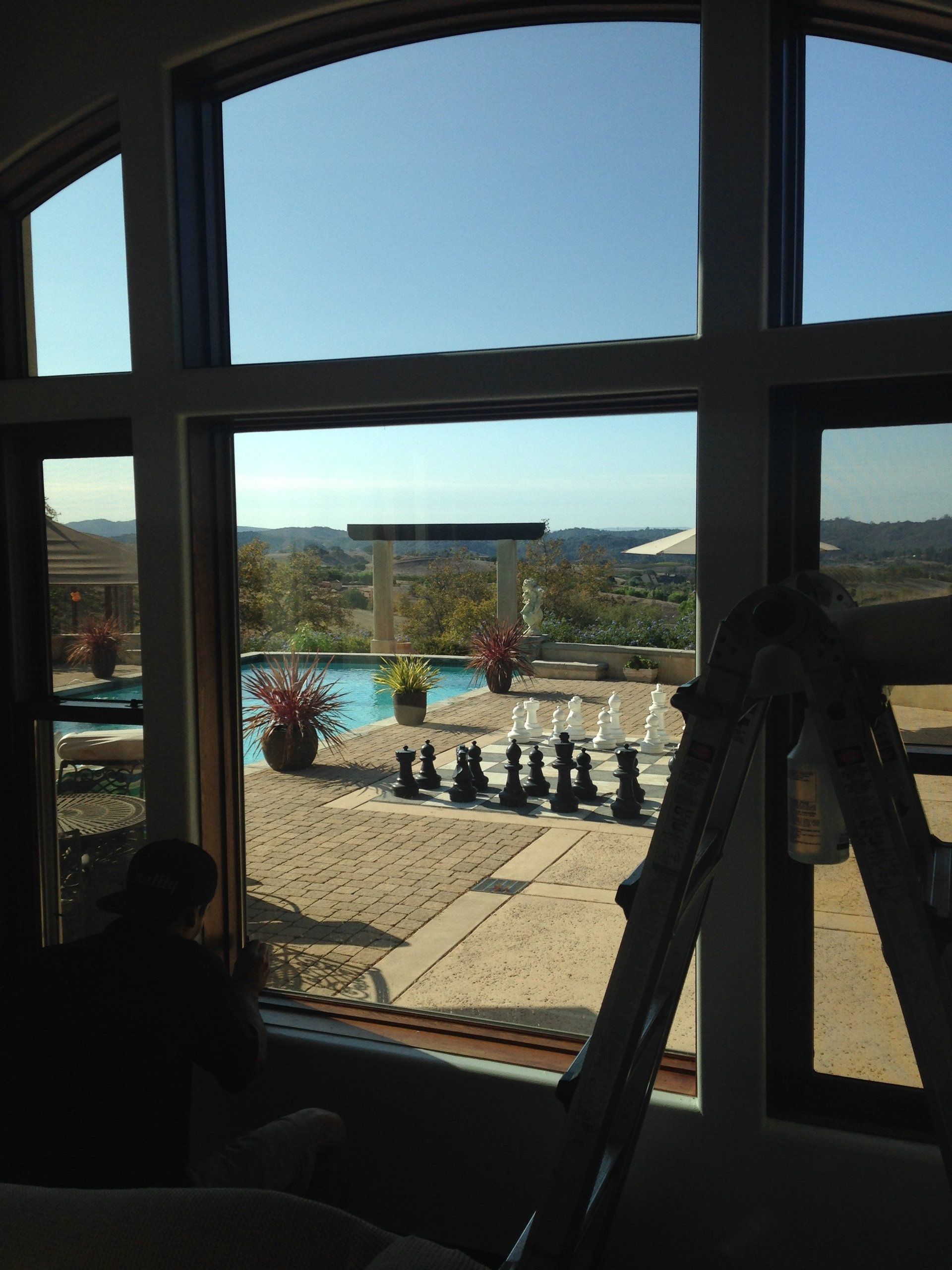 View through a large window of a courtyard with people seated near a fountain and a ladder inside the room