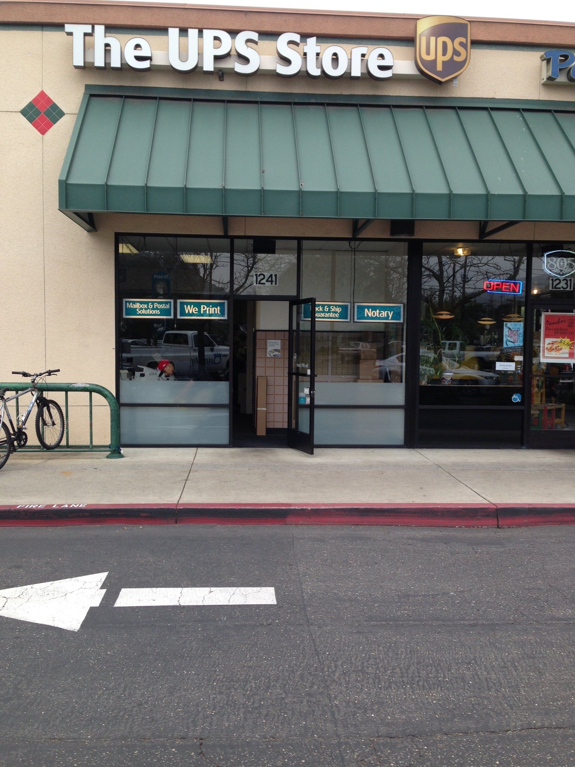 The UPS Store storefront with green awning and glass doors on a city sidewalk.