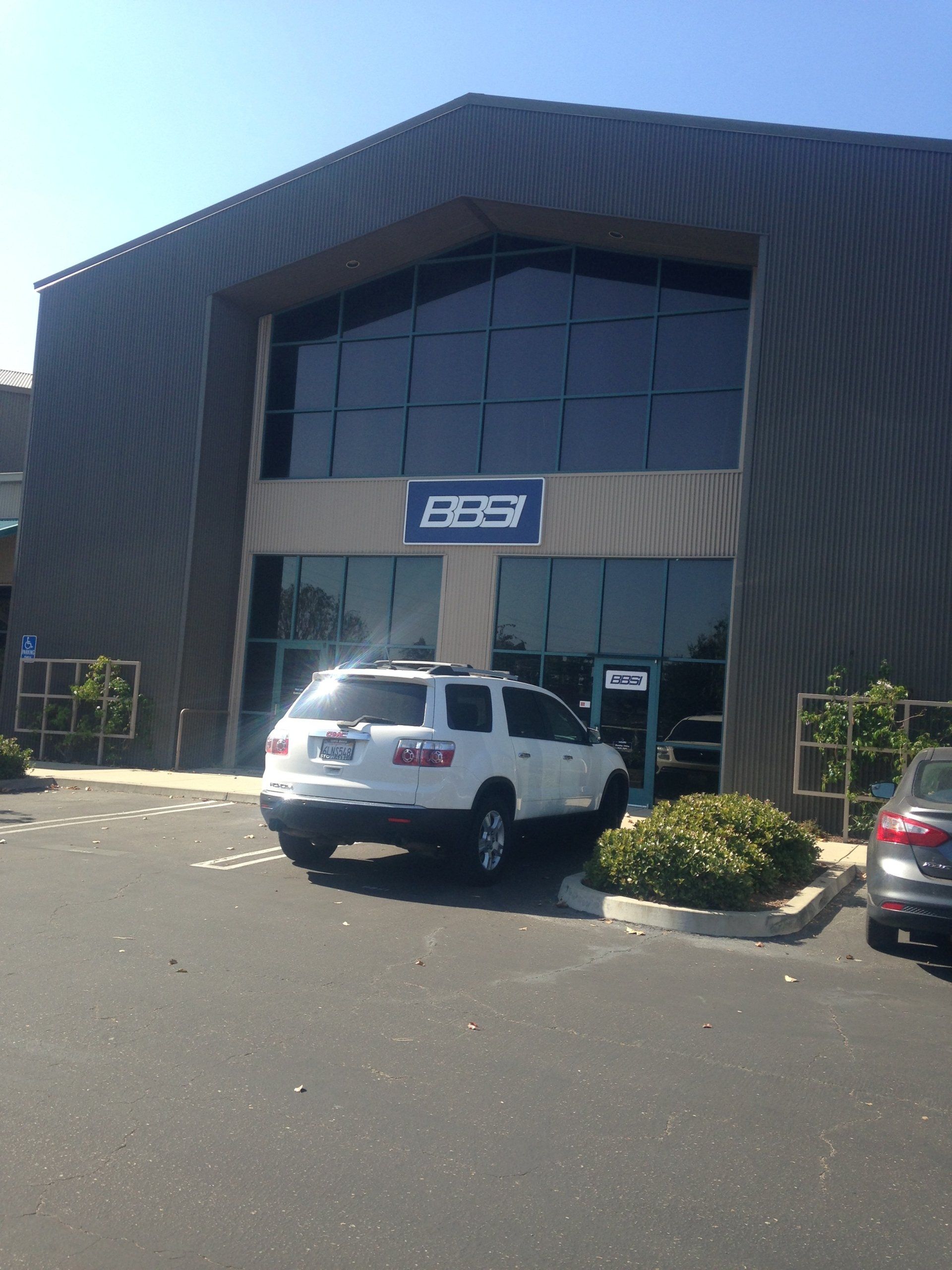 Front of a modern industrial building with an ESS sign and parked vehicles outside.