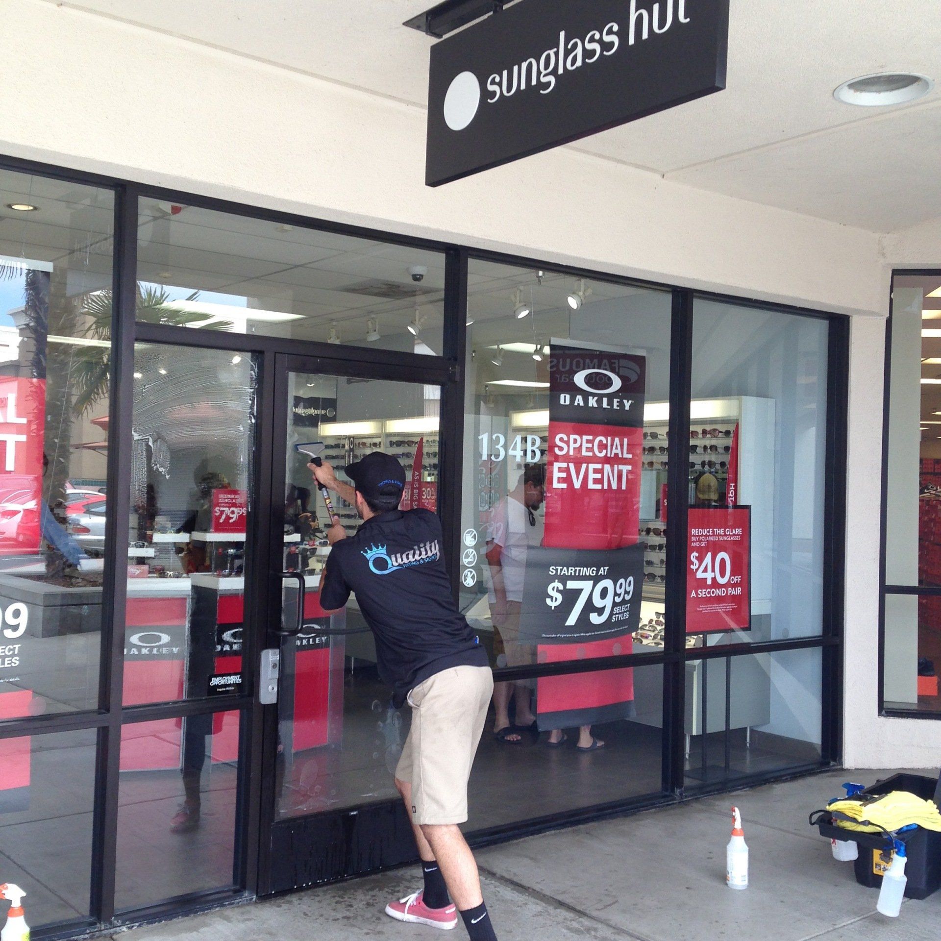 Person opening the Sunglass Hut store door in a shopping center, with sale signs in the window.