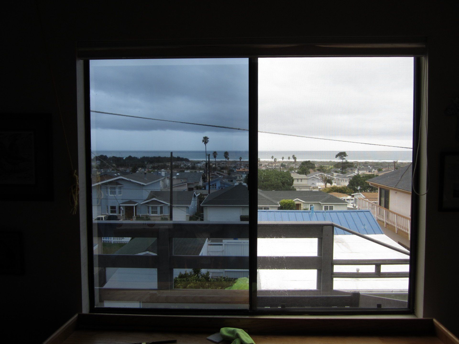 View through a window of rooftops and ocean under a cloudy sky