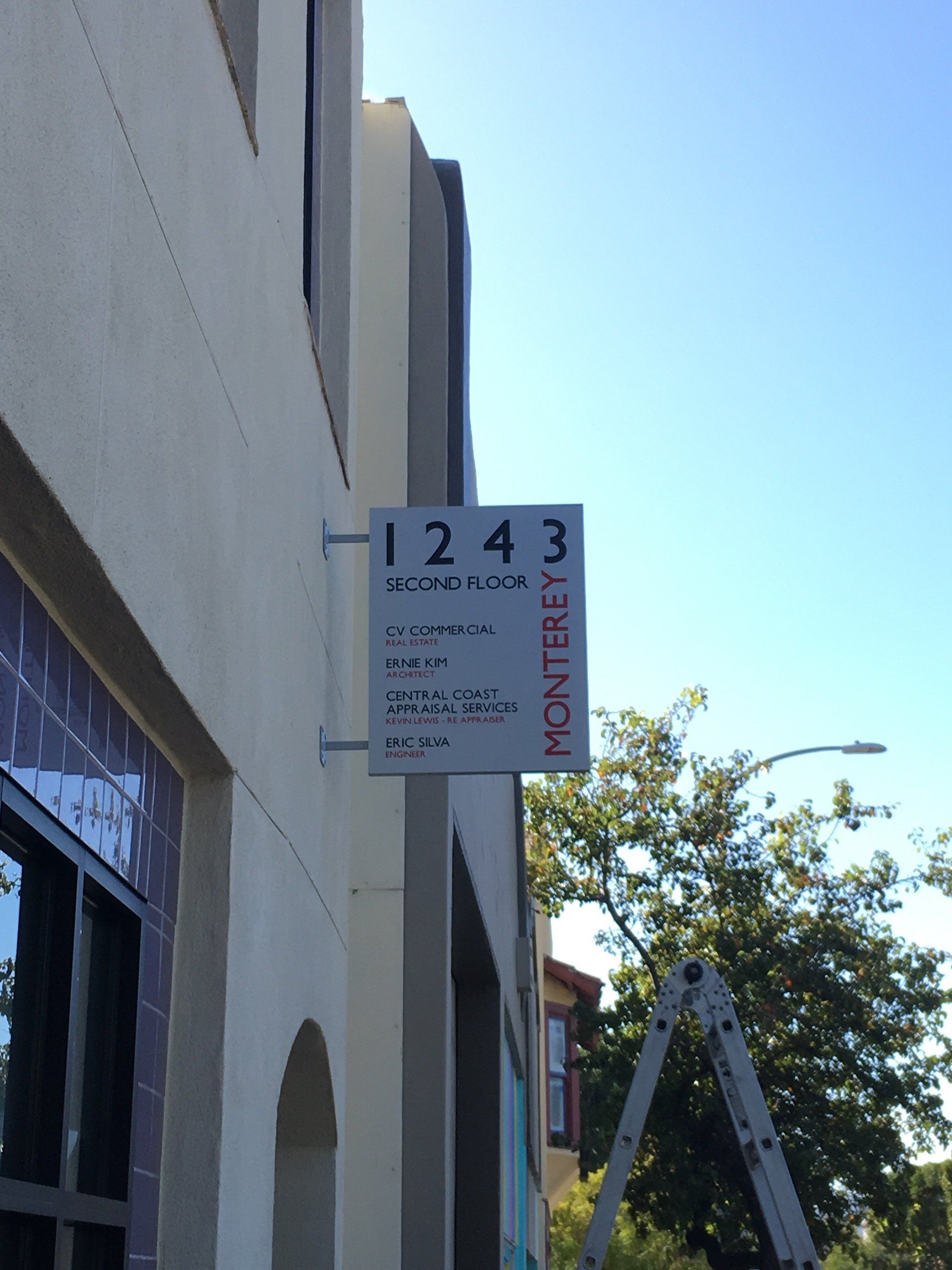 Storefront sign reading “1243” on a building exterior, with a ladder nearby under a clear blue sky.
