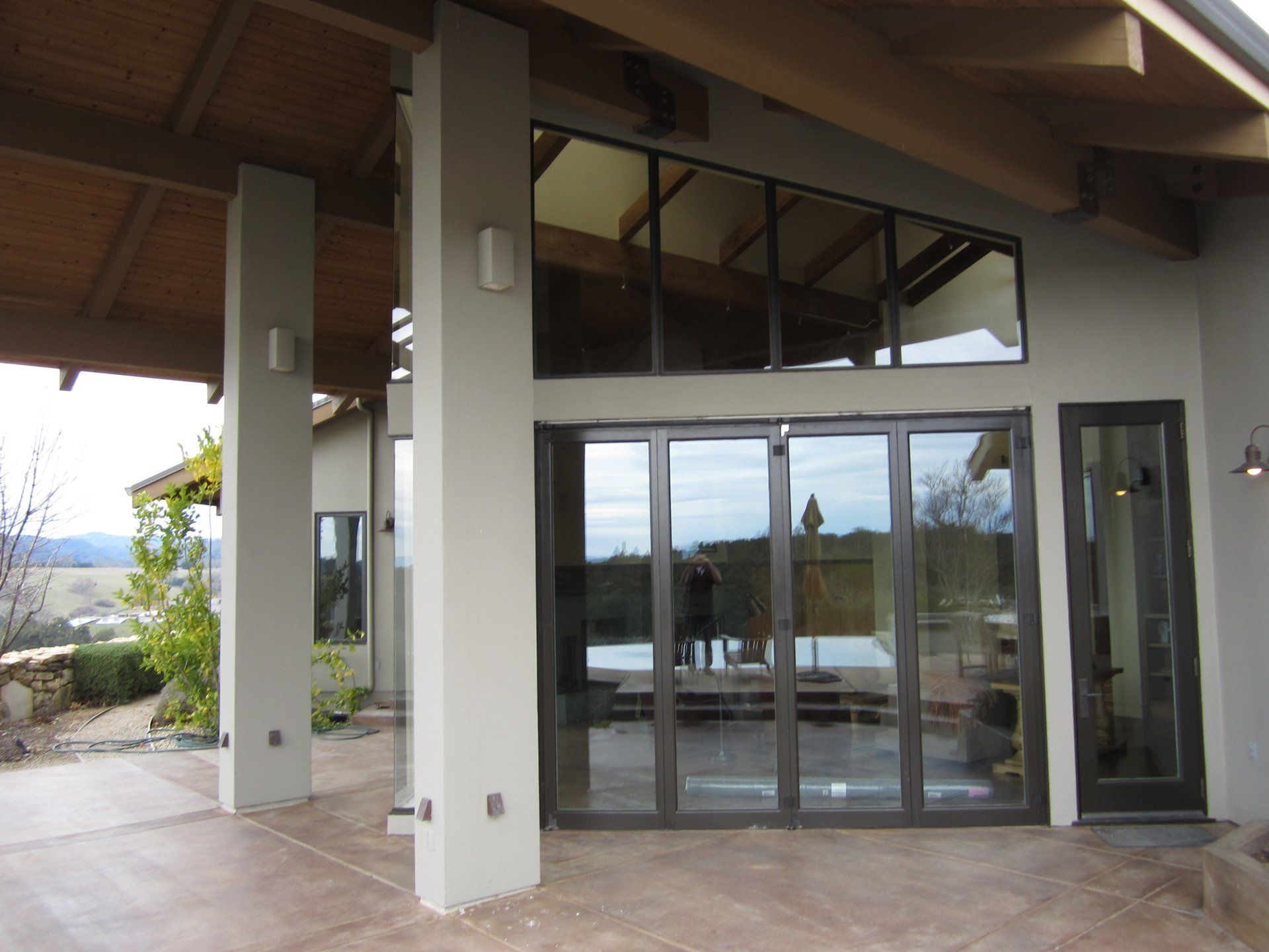 Modern house exterior with glass sliding doors, covered patio, and view of the landscape beyond