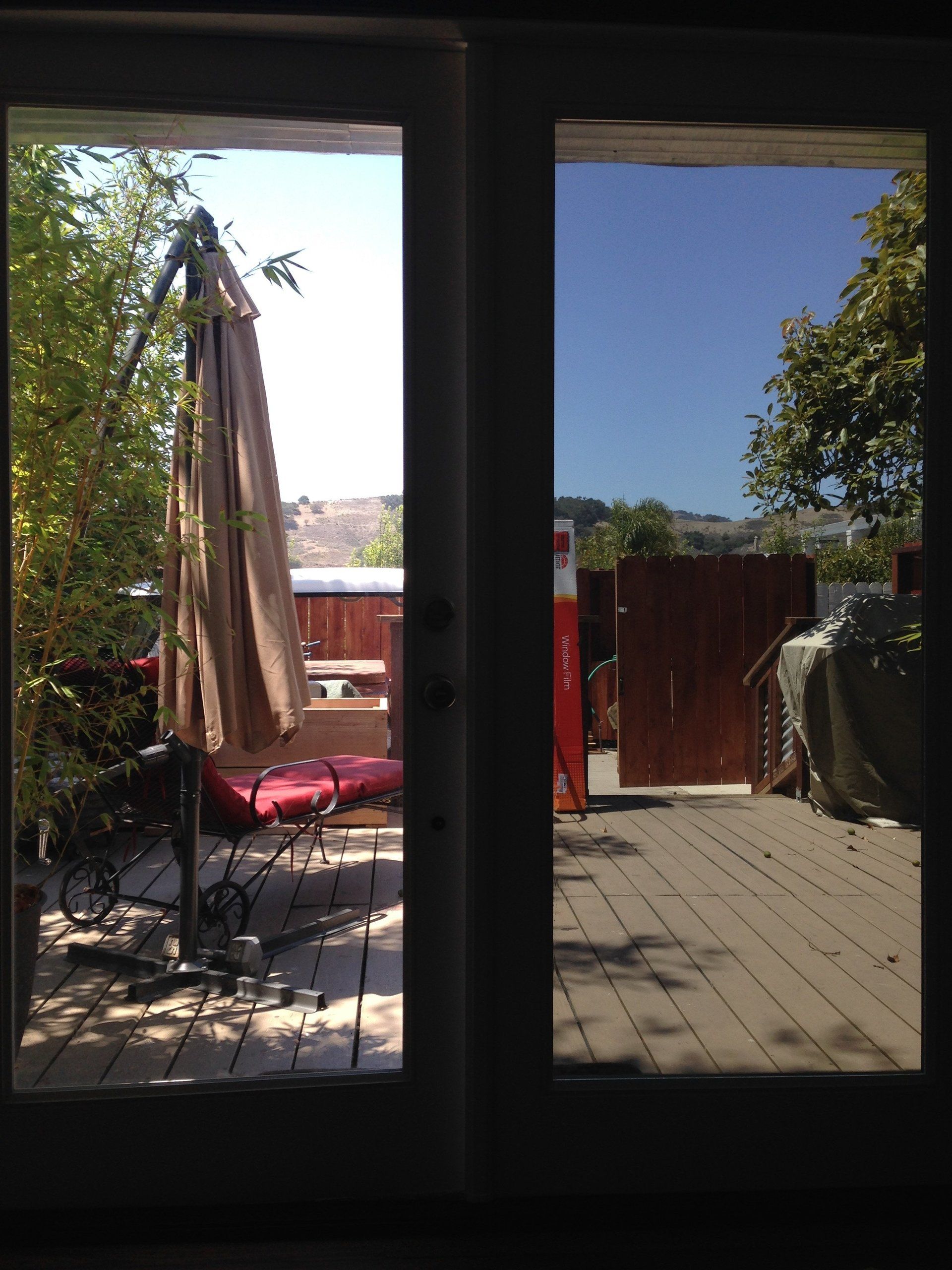 Patio seen through open doors, with a table, umbrella, chairs, and bright blue sky beyond.
