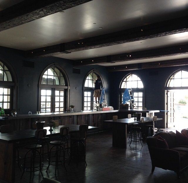 Dim, empty bar interior with arched windows, dark walls, and long counter seating