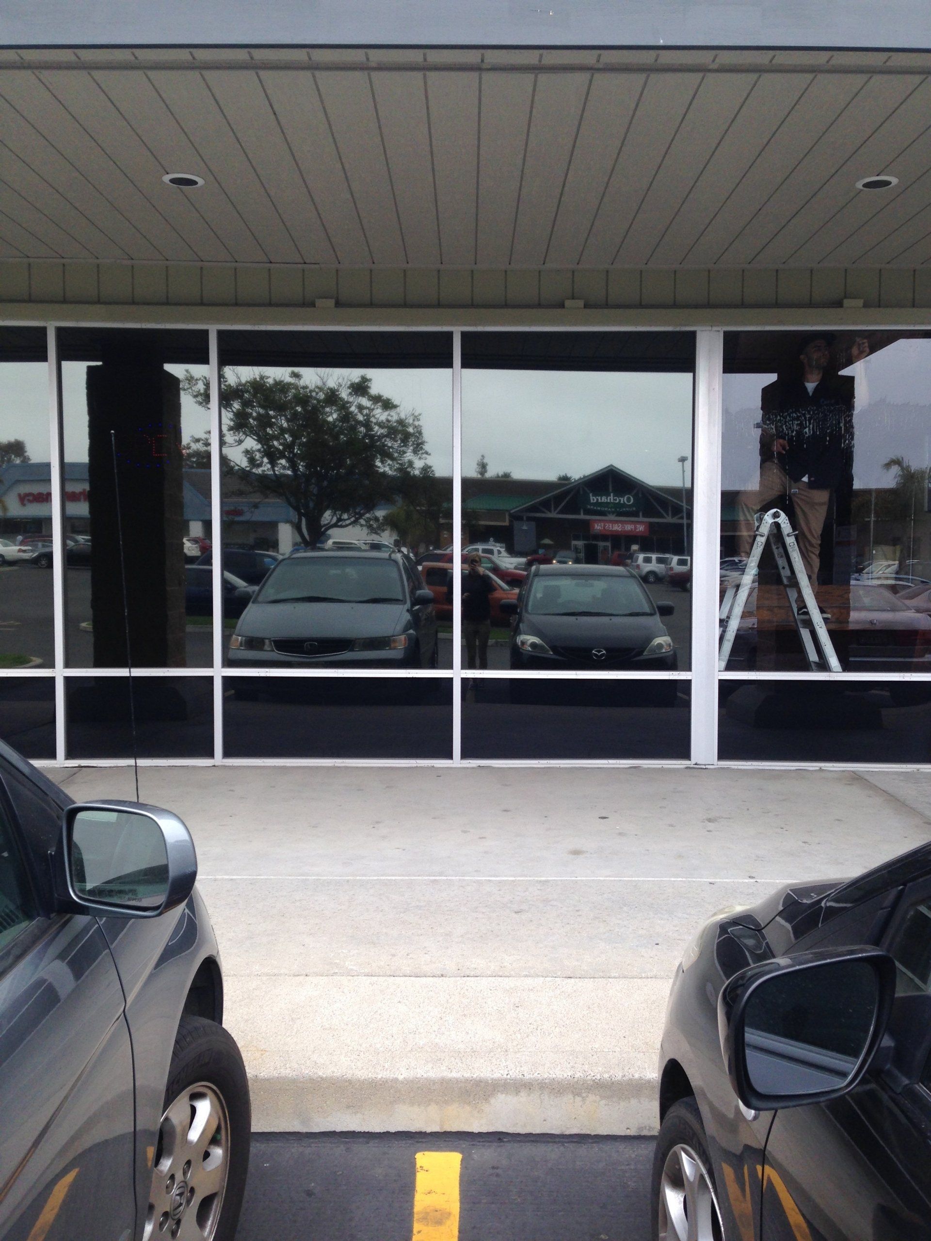 Storefront windows reflecting parked cars and a ladder outside under an overhang
