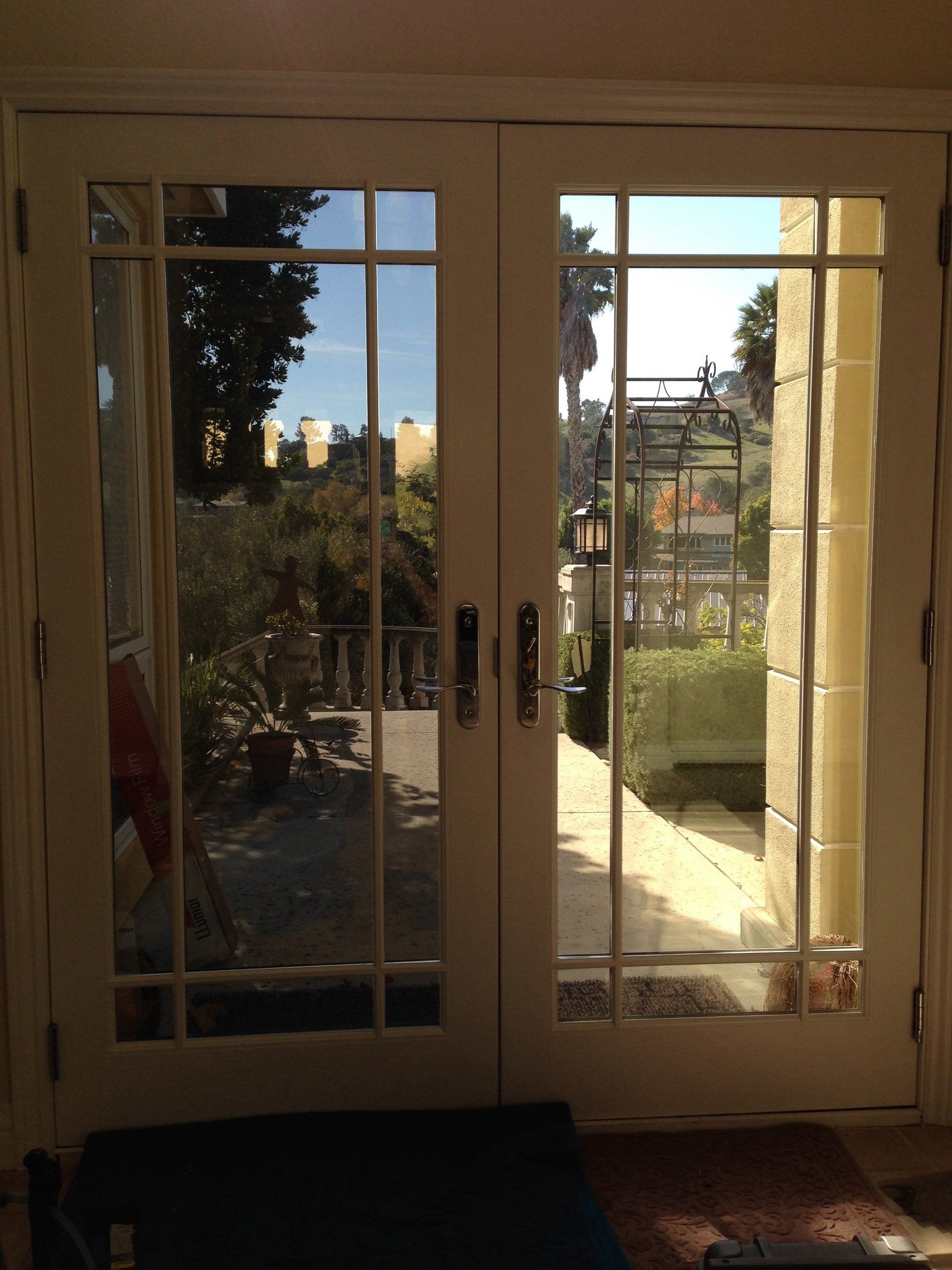 French doors opening to a sunlit garden with trees and a stone patio