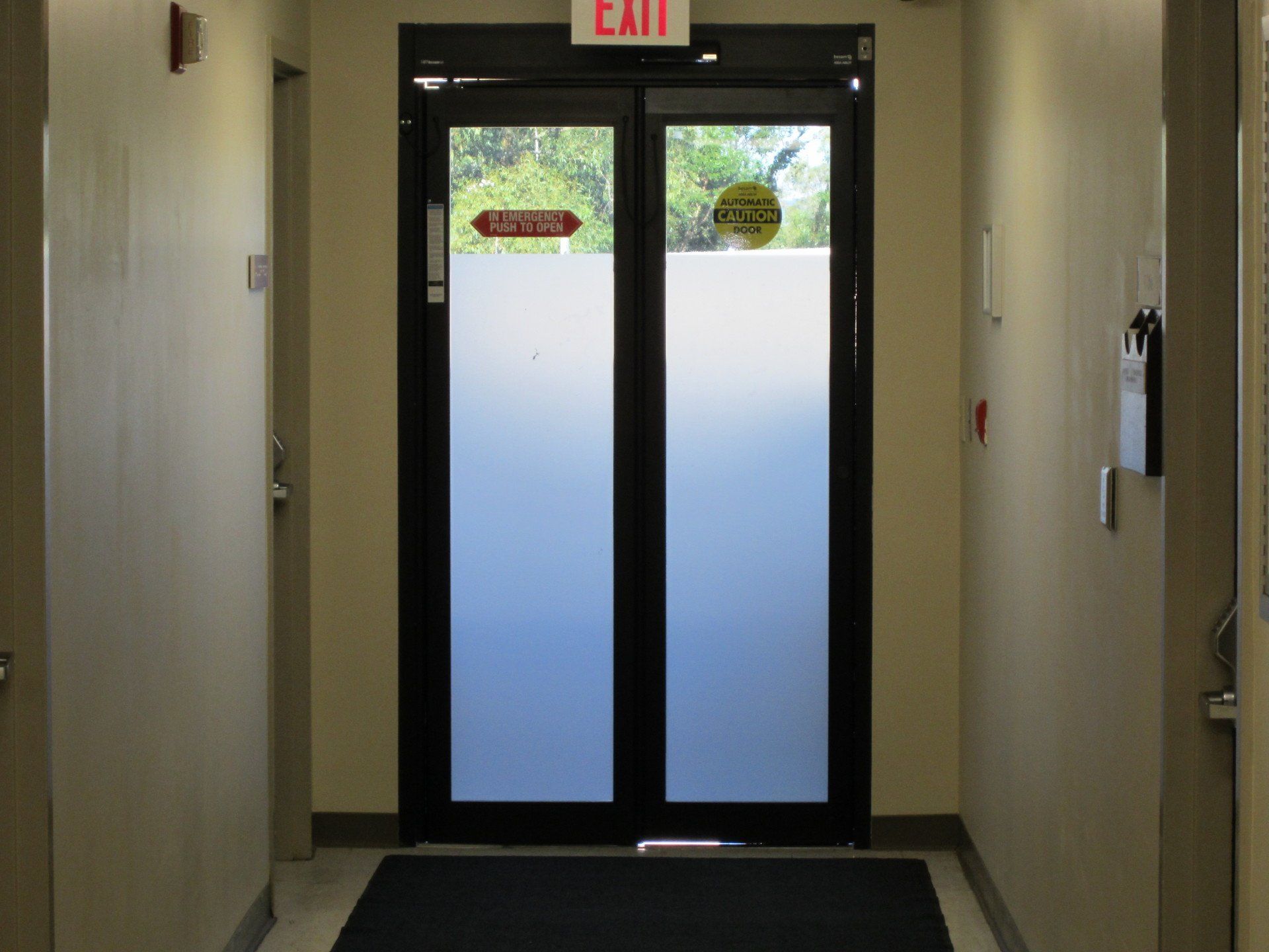 Hallway with double glass exit doors and red EXIT sign above them.