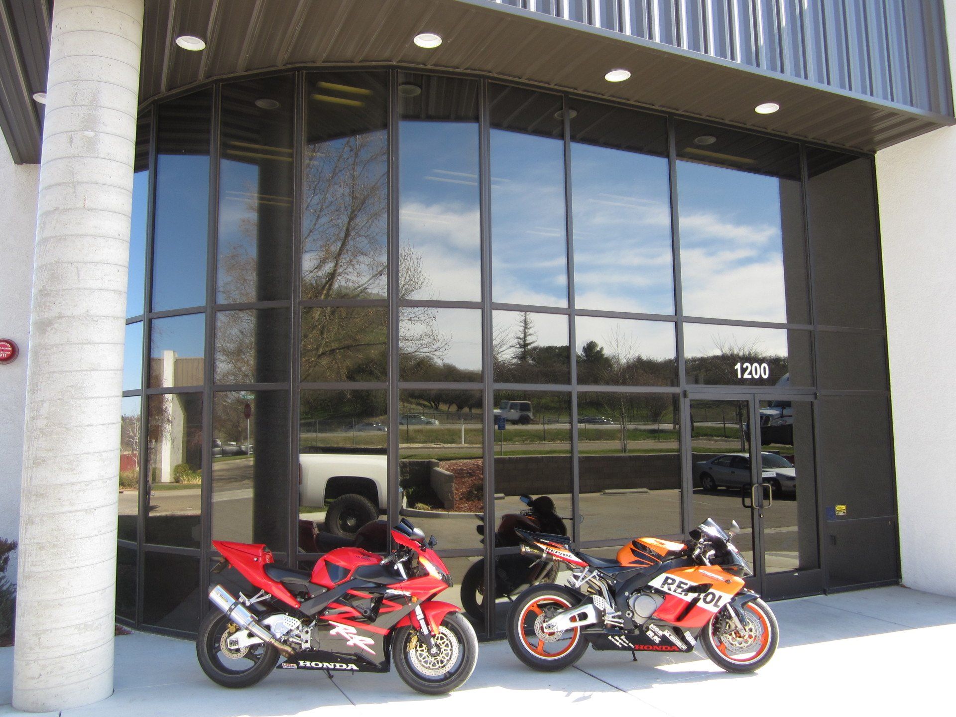 Two sport motorcycles parked outside a glass storefront with reflective windows
