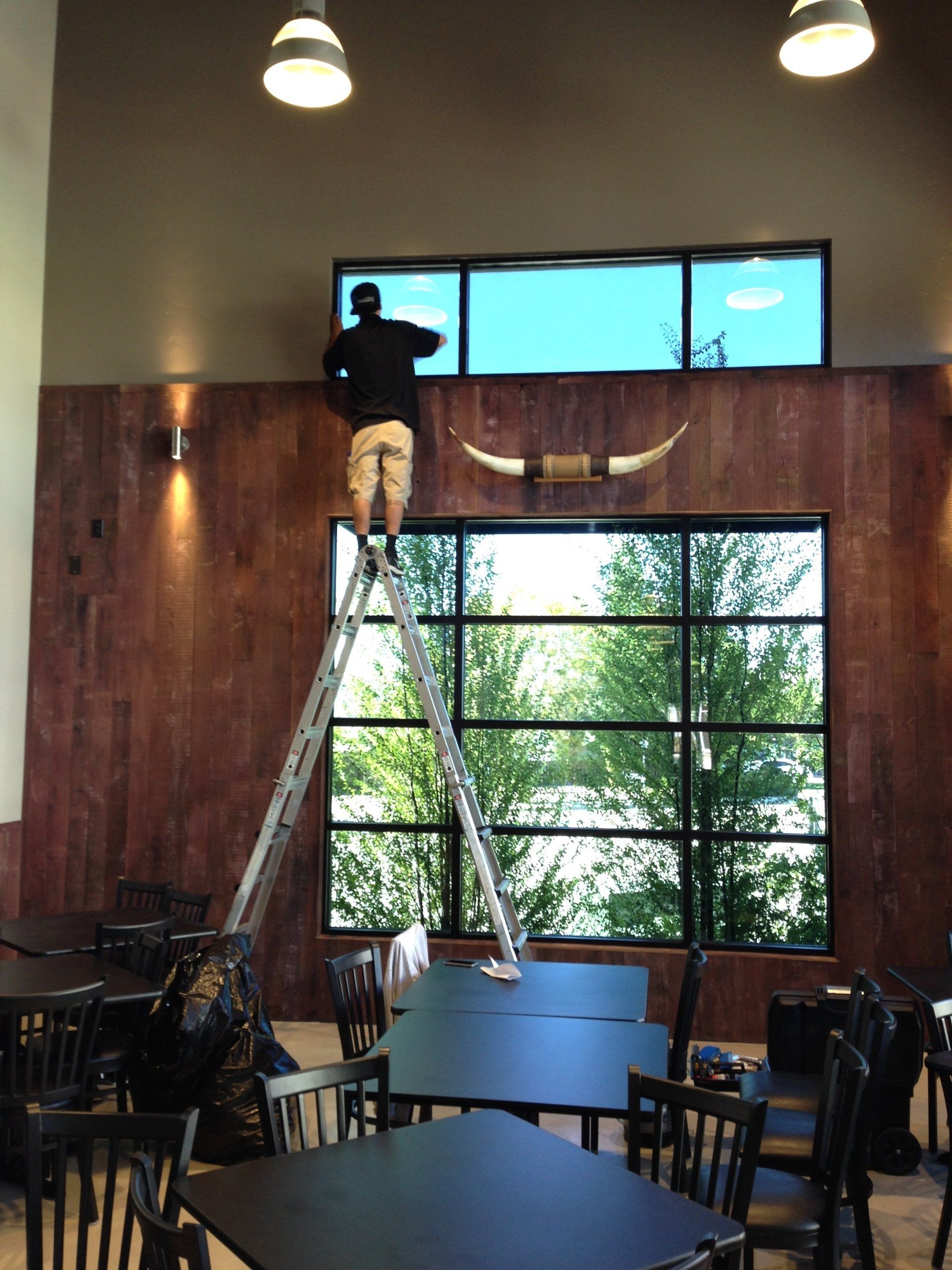 Person on a ladder installing or adjusting a window in a café with large panes and wooden walls