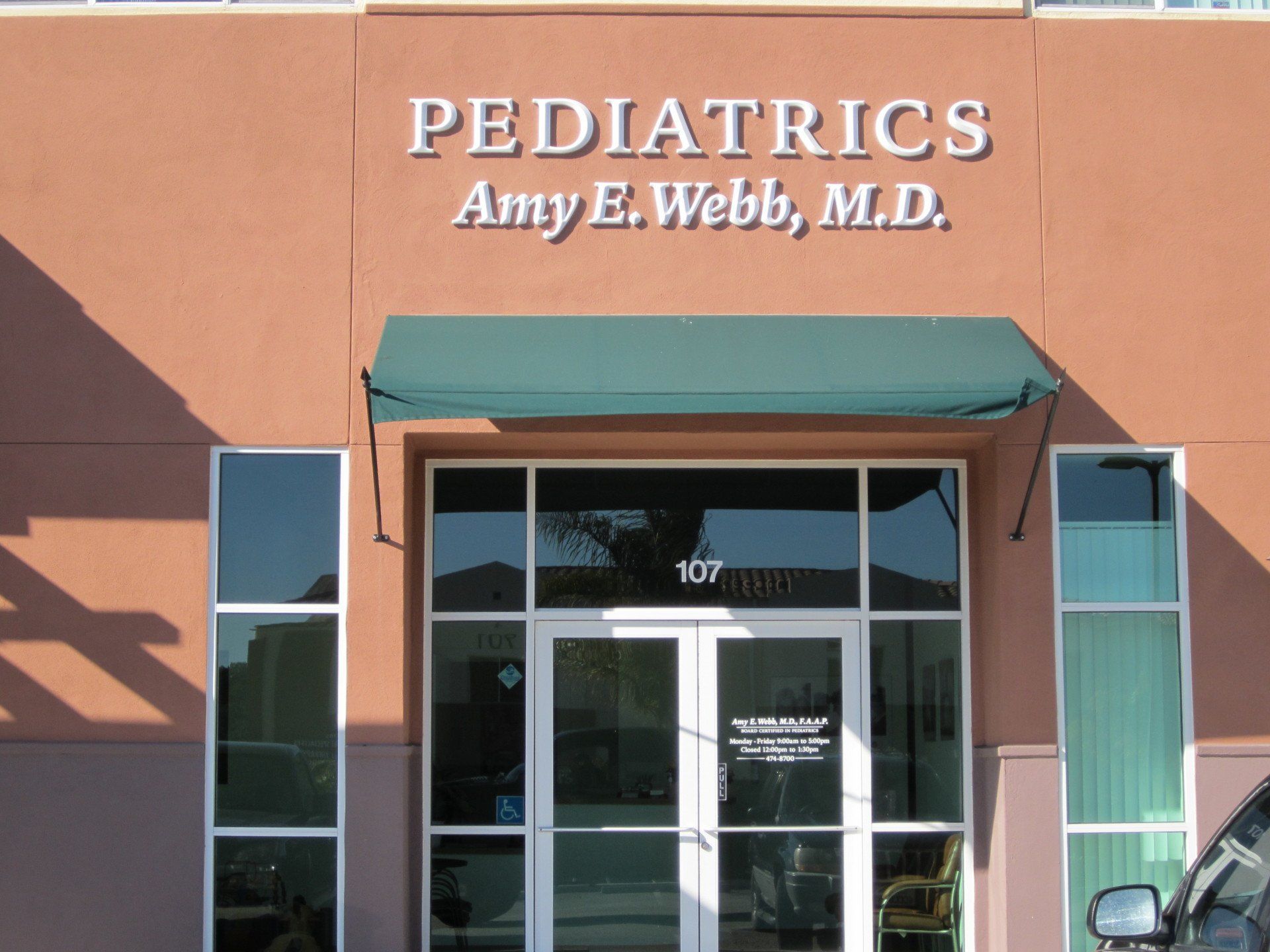 Pediatrics office entrance with orange facade, teal awning, and glass doors for Amy E. Webb, M.D.