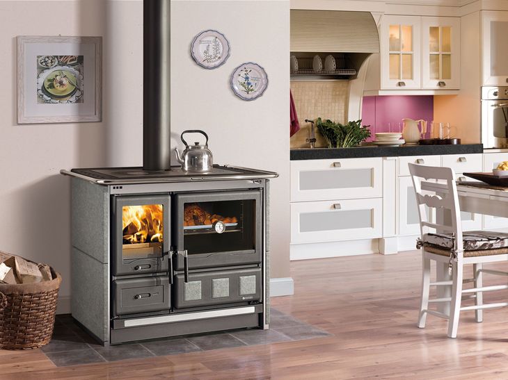 Stufa a legna moderna di colore nero con fuoco acceso in una luminosa cucina-sala da pranzo.